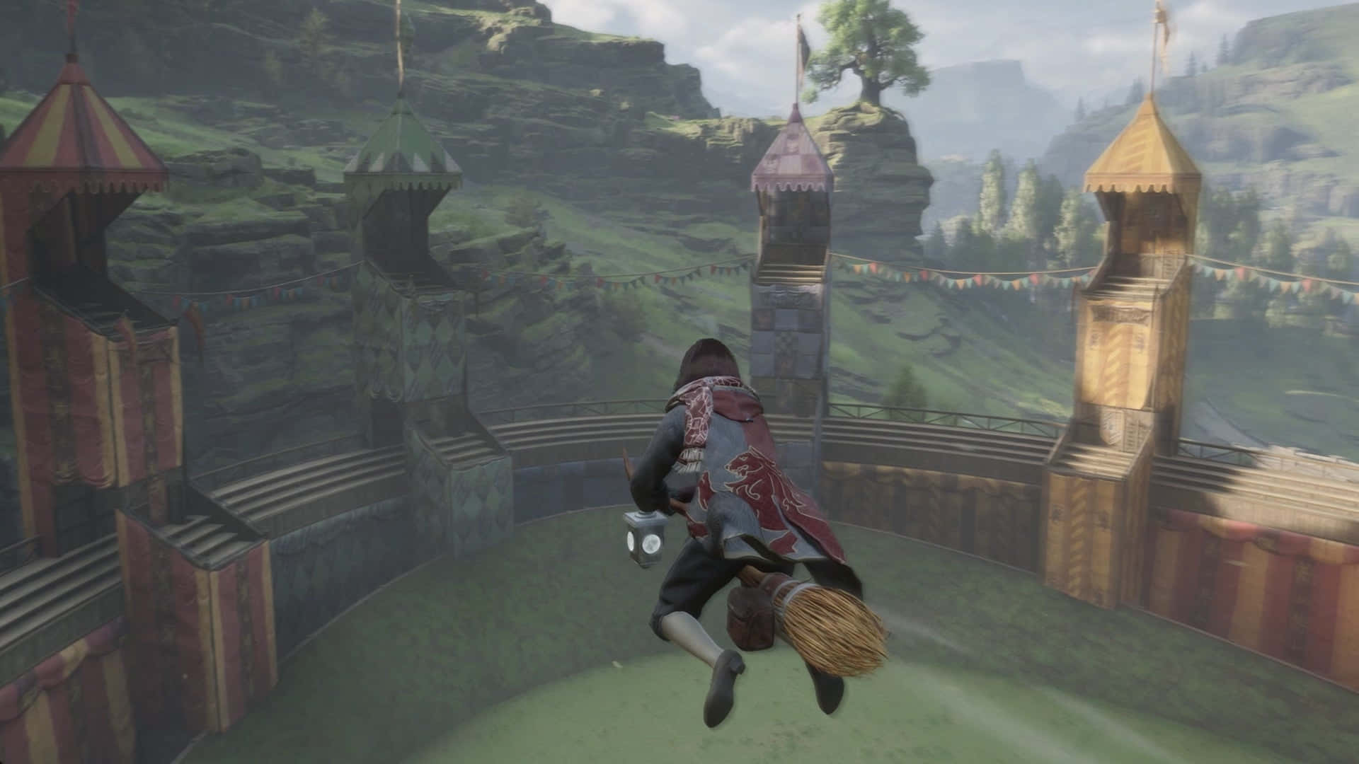 The Hogwarts Quidditch Pitch 桌布 壁紙 — 一位巫師騎著掃帚飛過一個圓形競技場，周圍是色彩繽紛的城堡塔樓，位於霧氣瀰漫的山谷中。