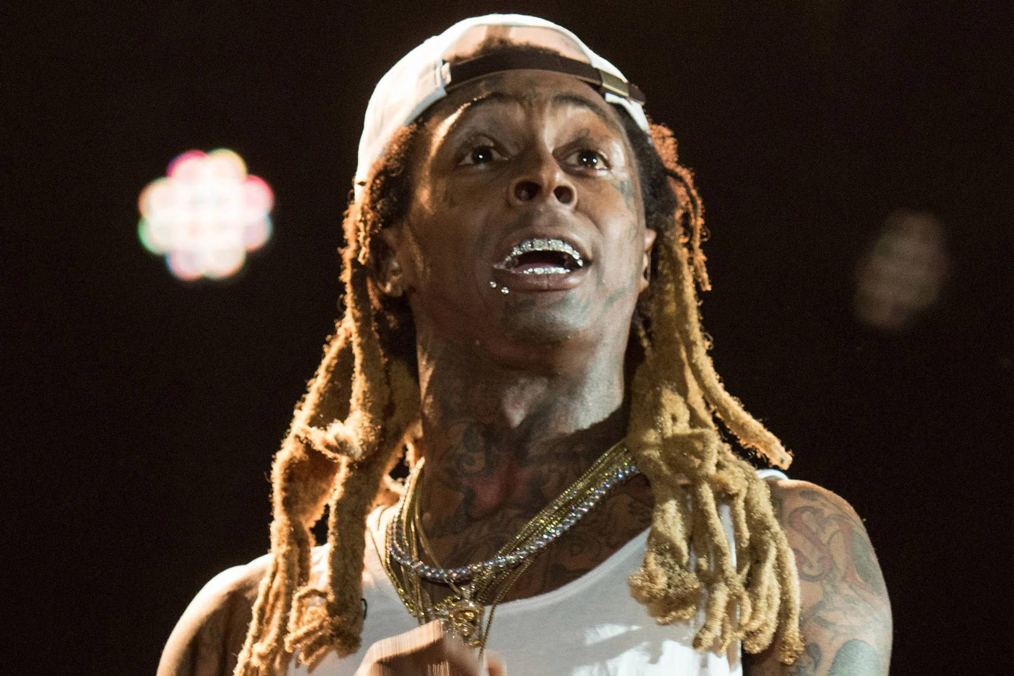 Lil Wayne 桌布 壁紙 — 一位帶有刺青、梳著辮子頭並戴著白色帽子的饒舌歌手在舞台燈光下表演的特寫。