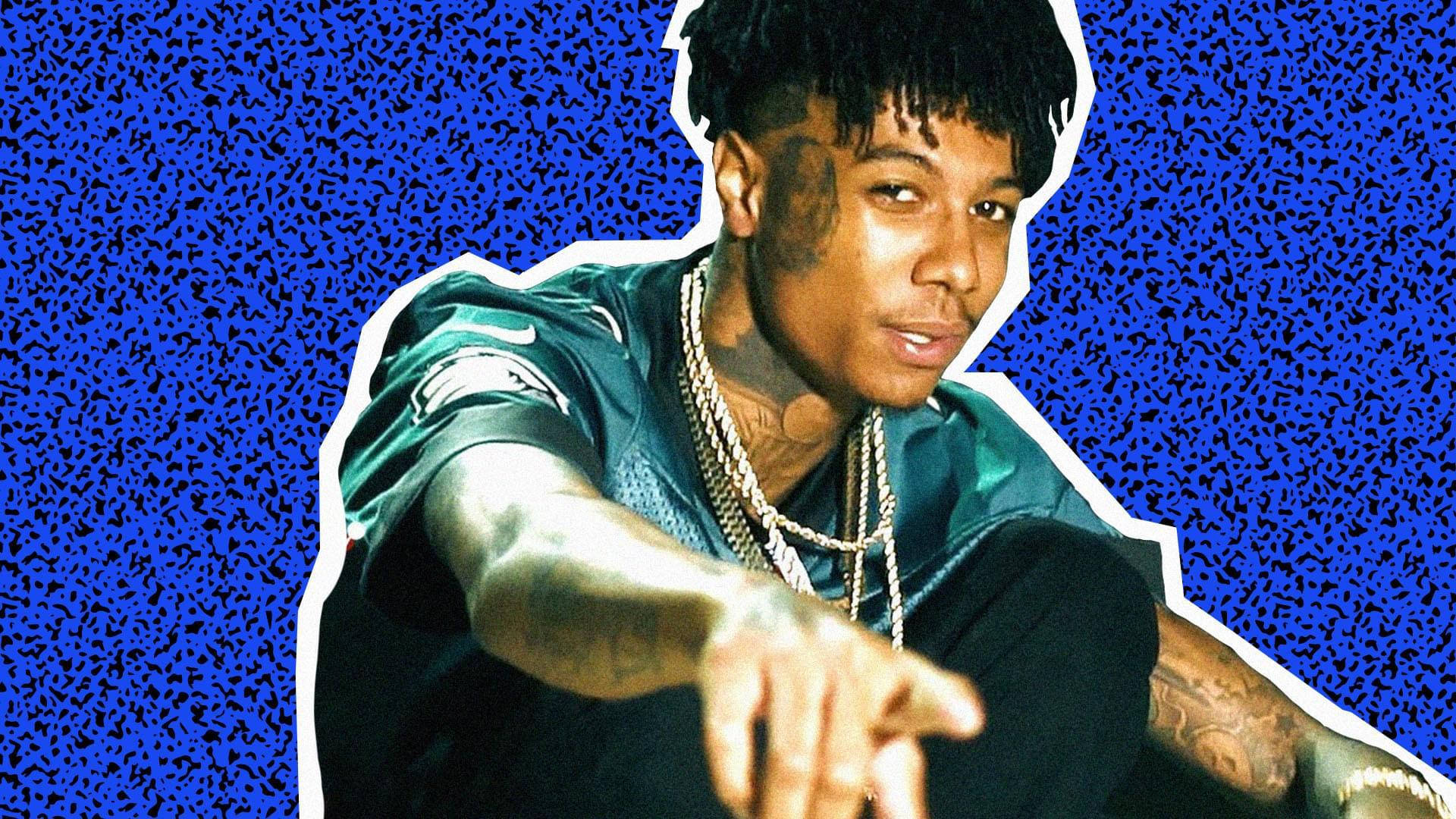 Celebrity 桌布 壁紙 — 一位帶有刺青和鏈條的年輕男子在充滿活力的藍色靜態背景前指向前方。