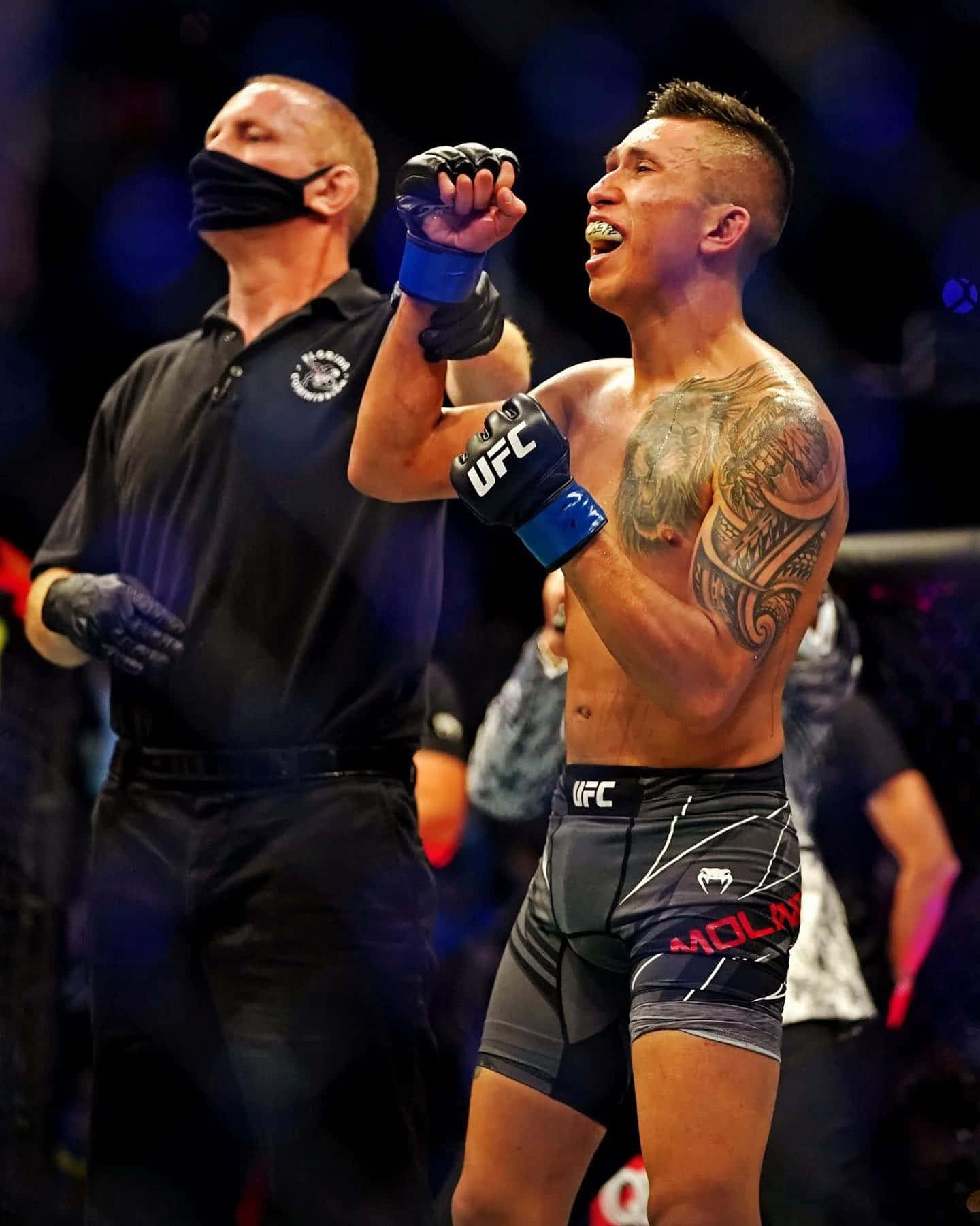 MMA 桌布 壁紙 — 一位帶有刺青的UFC勝利拳手在明亮的場館燈光下於八角籠內高舉拳頭慶祝勝利。