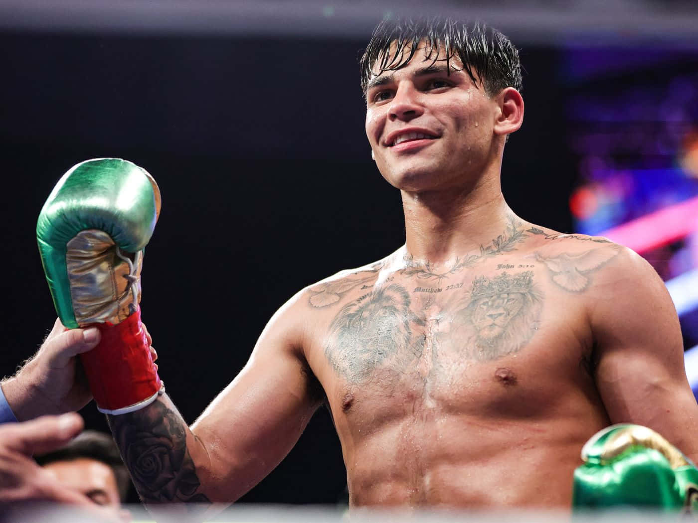 Ryan Garcia 桌布 壁紙 — 一位帶有獅子刺青的勝利拳擊手在擂台上微笑著舉起他的綠色和紅色手套。