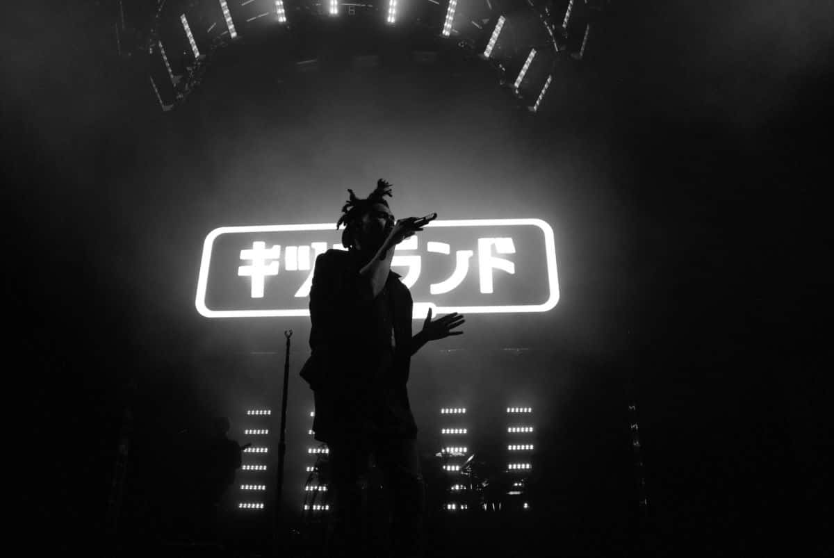 一位音樂家在明亮的燈光下表演，身後有日文字。