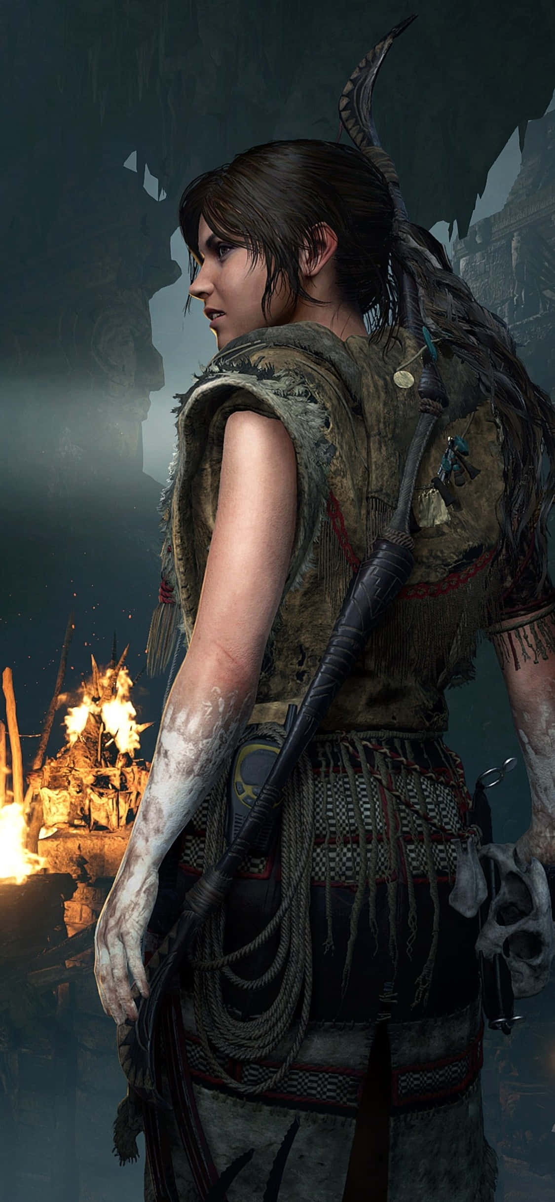 Pixel 3 Shadow Of The Tomb Raider 桌布 壁紙 — 一位帶有部落紋身和弓箭的戰士站在黑暗的洞穴中，身後燃燒的火焰將溫暖的光線投射在她飽經風霜的皮膚上。