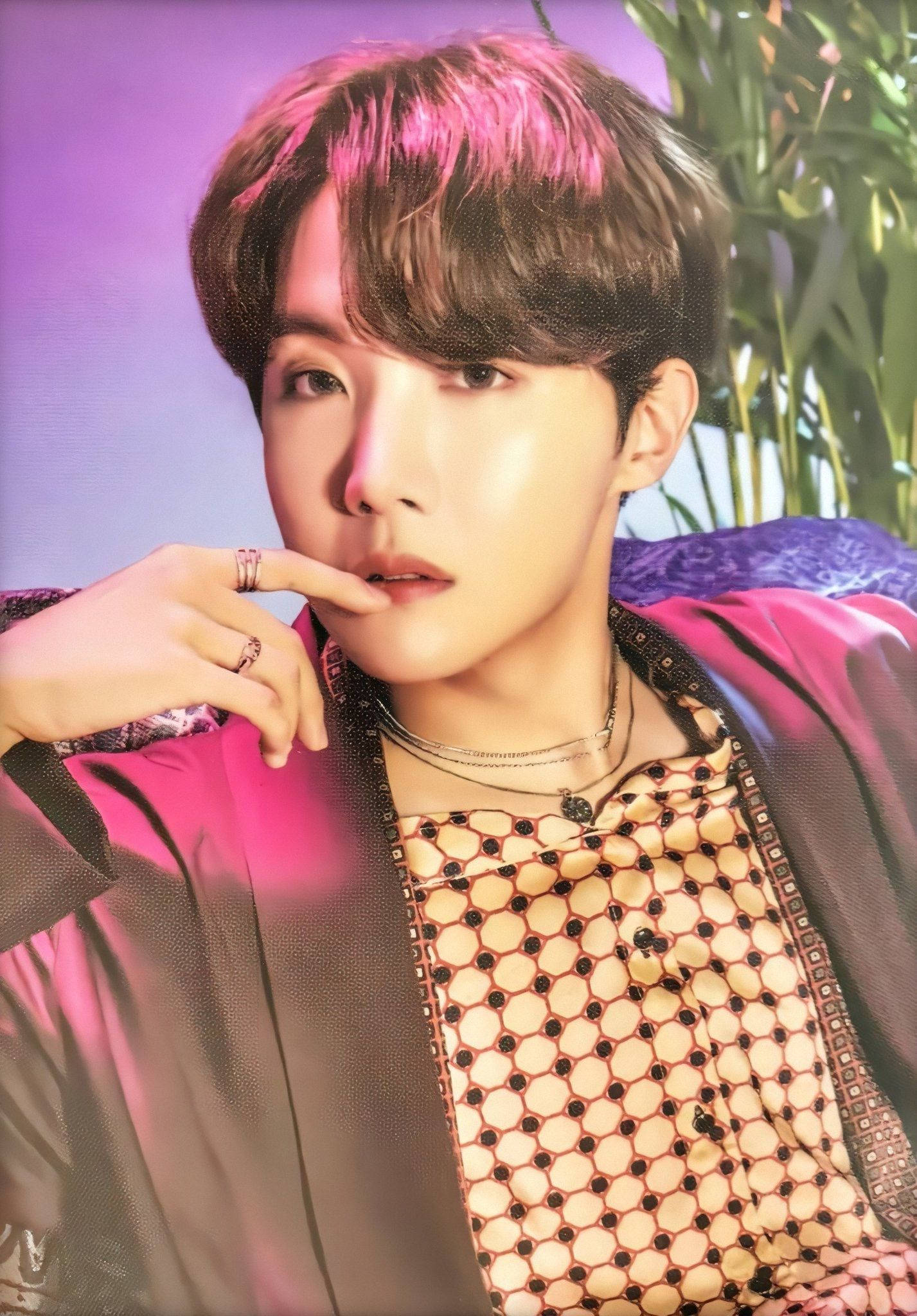 Cute Bts 桌布 壁紙 — 一位帶粉紅色頭髮的年輕男子在紫色背景和綠色樹葉前沉思地擺姿勢。