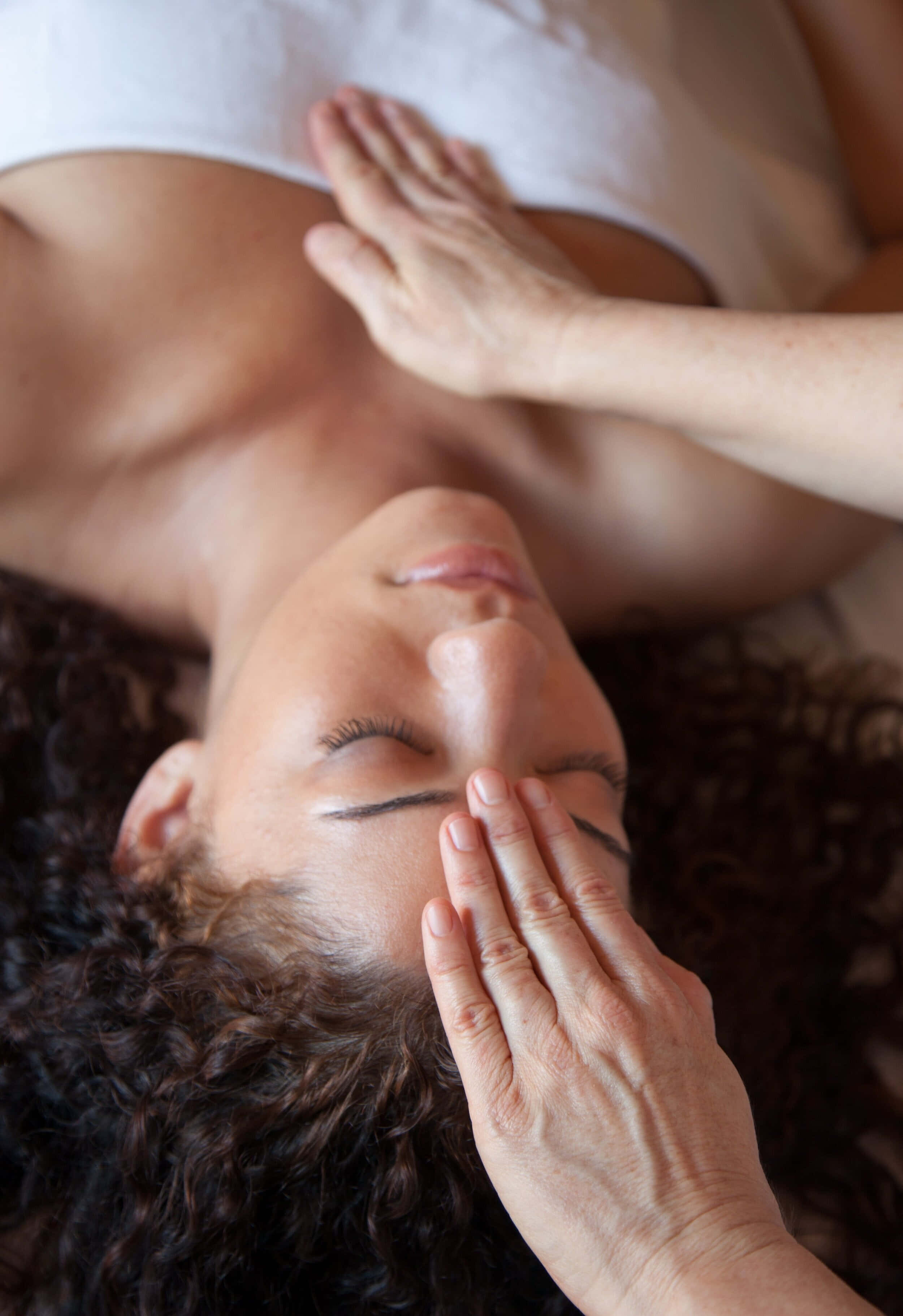 Reiki 桌布 壁紙 — 一位平靜的深色捲髮女性在寧靜的水療環境中接受治療師的溫和面部按摩。