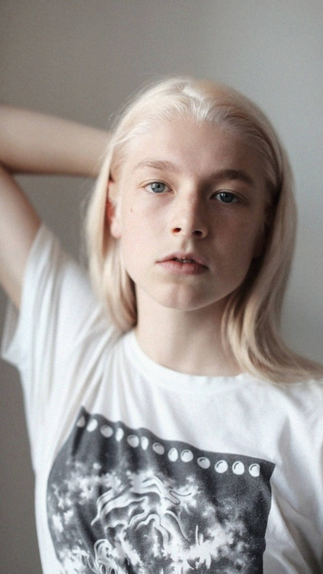 Hunter Schafer 桌布 壁紙 — 一位年輕人有著鉑金色頭髮和藍色眼睛，直接看著鏡頭，身穿帶有黑色圖案印花的白色T恤。