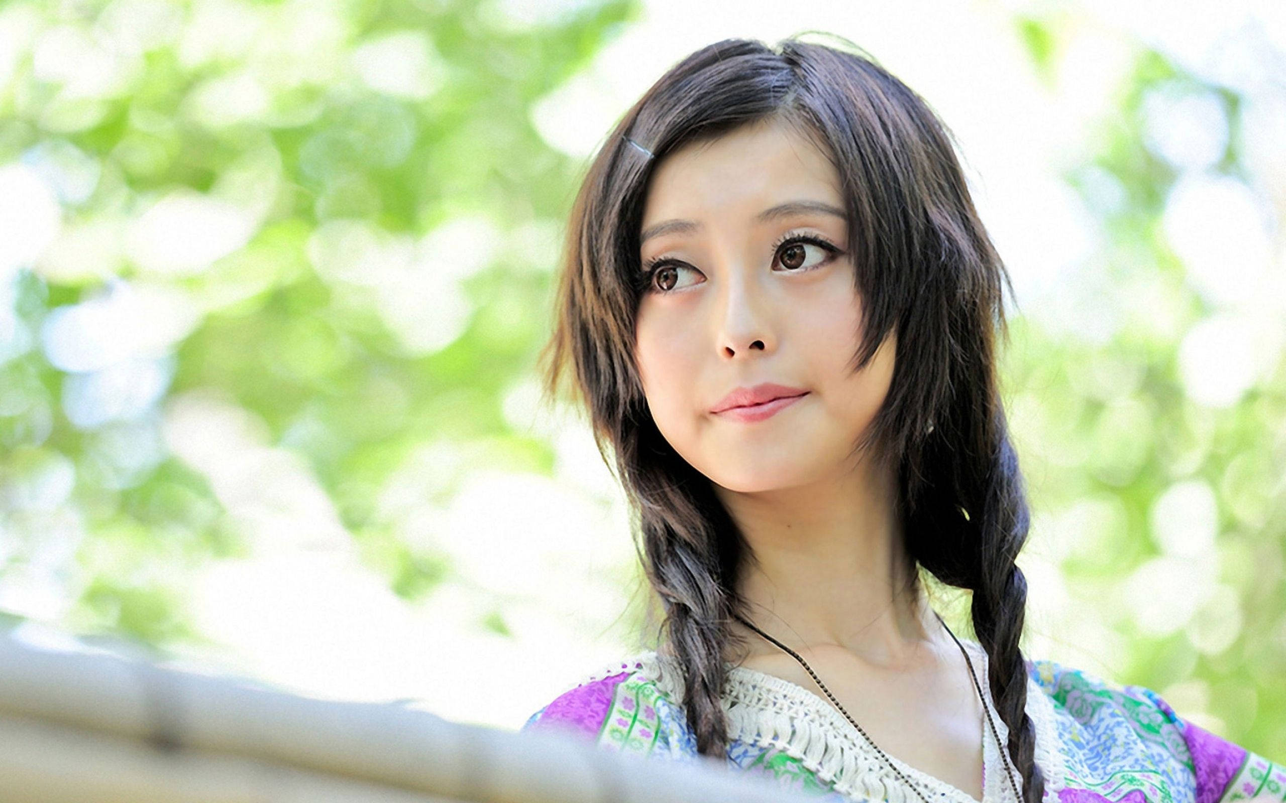 美女 桌布 壁紙 — 一位年輕女子，編著深色辮子，在明亮的綠色葉子背景前若有所思地向上凝視。