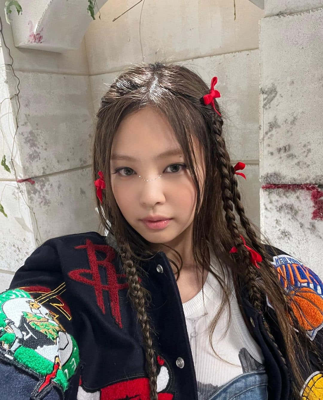 BLACKPINK 桌布 壁紙 — 一位年輕女子，辮子上繫著紅色絲帶，身穿一件打滿補丁的夾克，靠著風化的石牆。