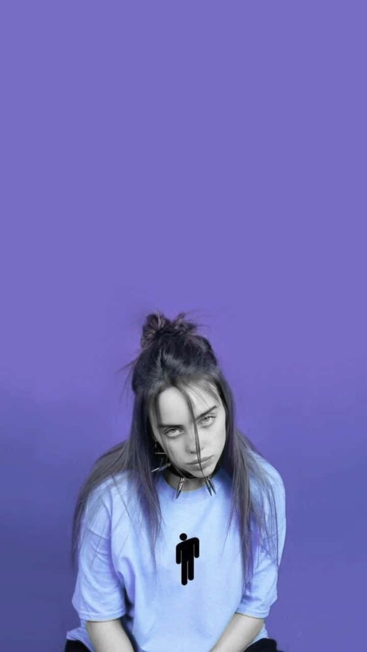 怪奇比莉 桌布 壁紙 — 一位年輕女子，頭髮凌亂，身穿淺藍色T恤，上面有黑色火柴人圖案，坐在純紫色背景前。