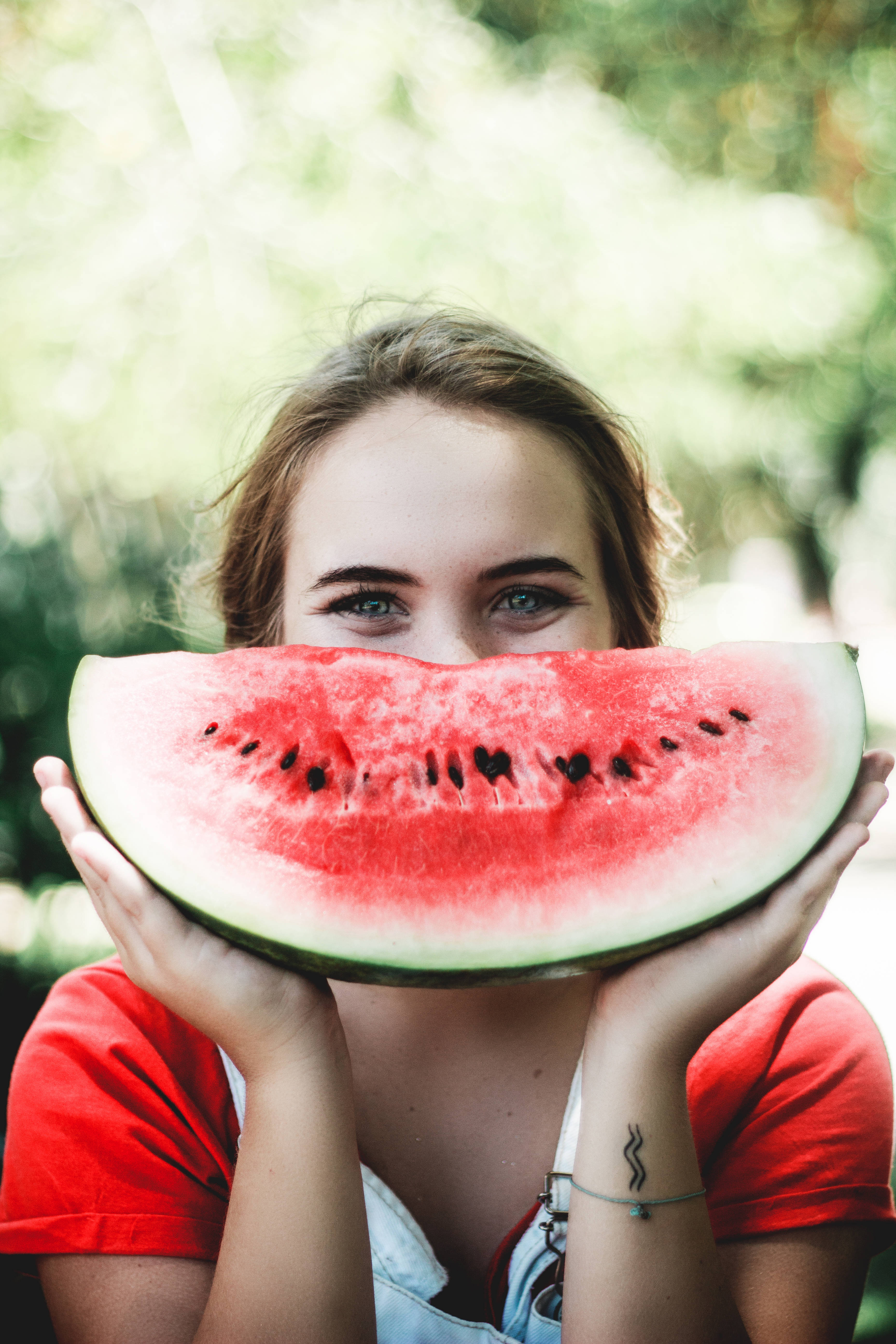 Fruit 桌布 壁紙 — 一位年輕女子手持多汁西瓜片遮住臉部，只露出明亮的綠色眼睛，背景是陽光明媚的綠色。
