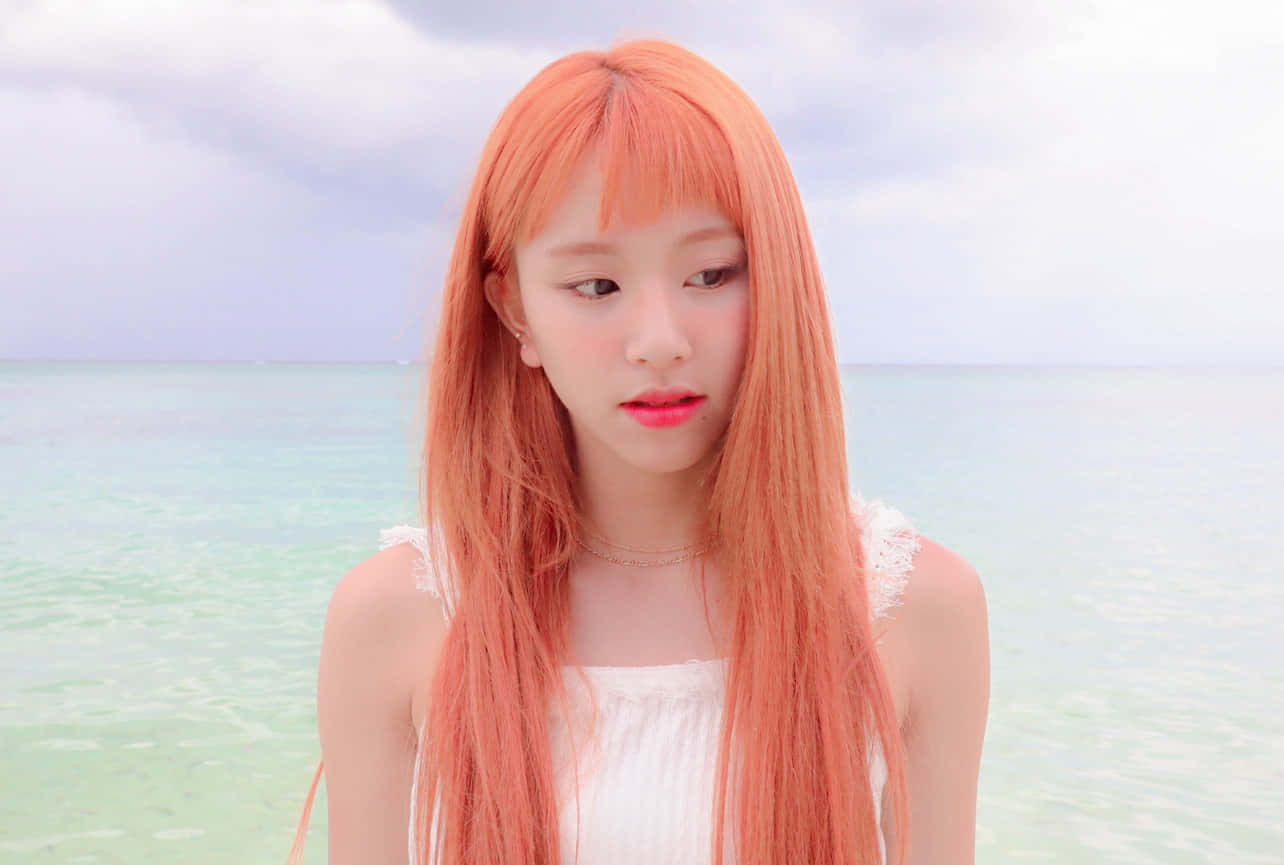 twice 桌布 壁紙 — 一位年輕女子擁有充滿活力的蜜桃色頭髮，站在平靜的碧綠海水旁，天空柔和多雲。