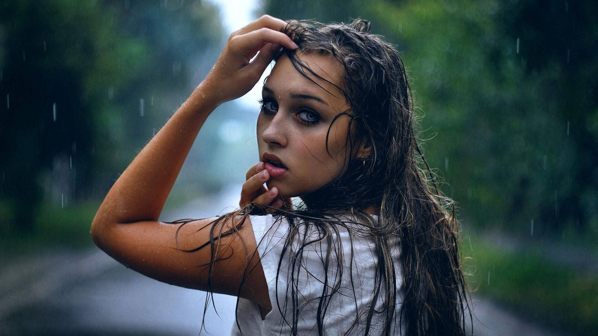Eyes 桌布 壁紙 — 一位年輕女子濕著頭髮站在雨中，手撩起髮絲，水滴在她周圍落下，形成一片翠綠的模糊背景。