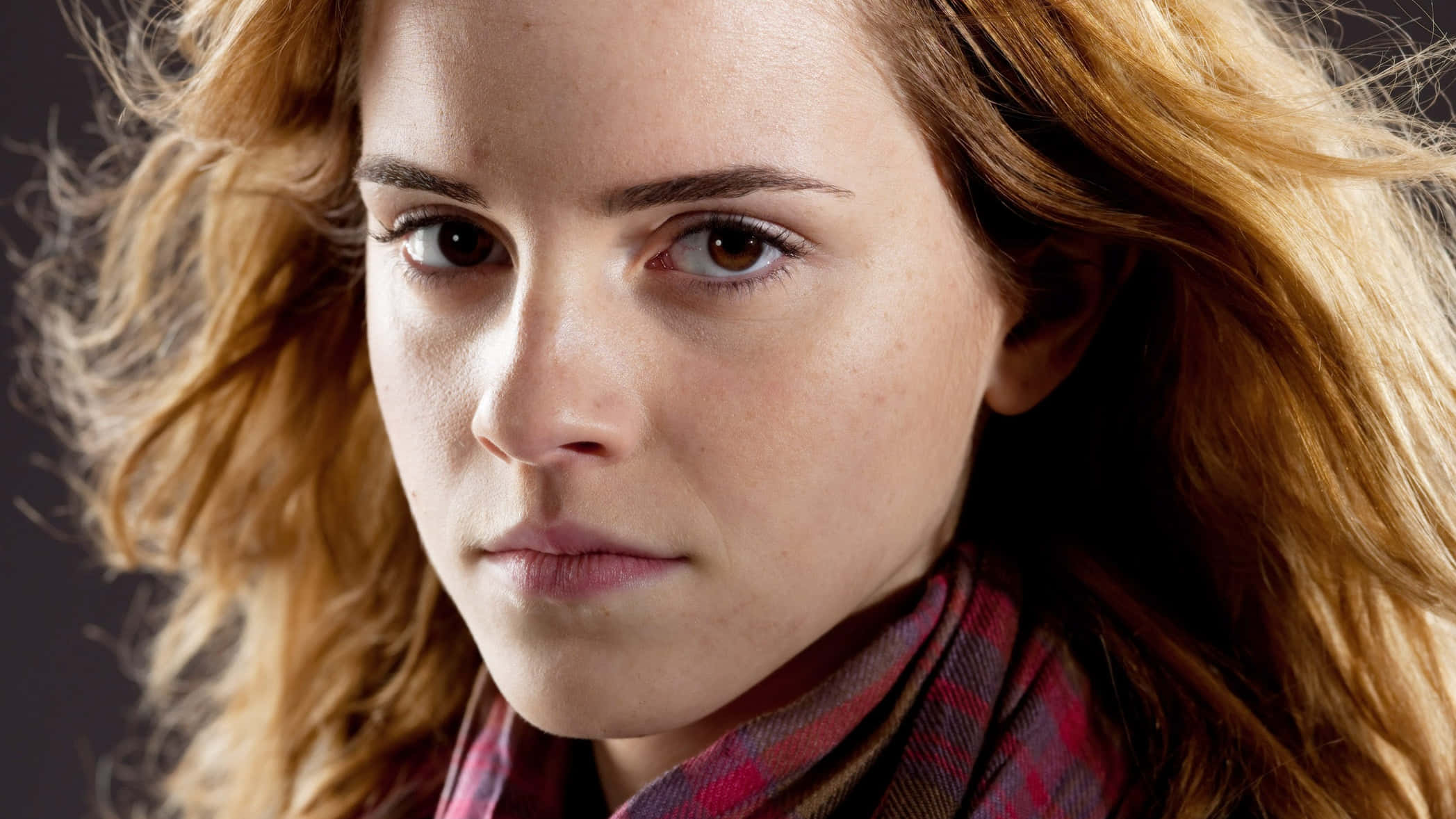 Emma Watson 桌布 壁紙 — 一位年輕女子的特寫肖像，擁有火紅的頭髮和強烈的棕色眼睛，在深色背景下戴著格子圍巾。