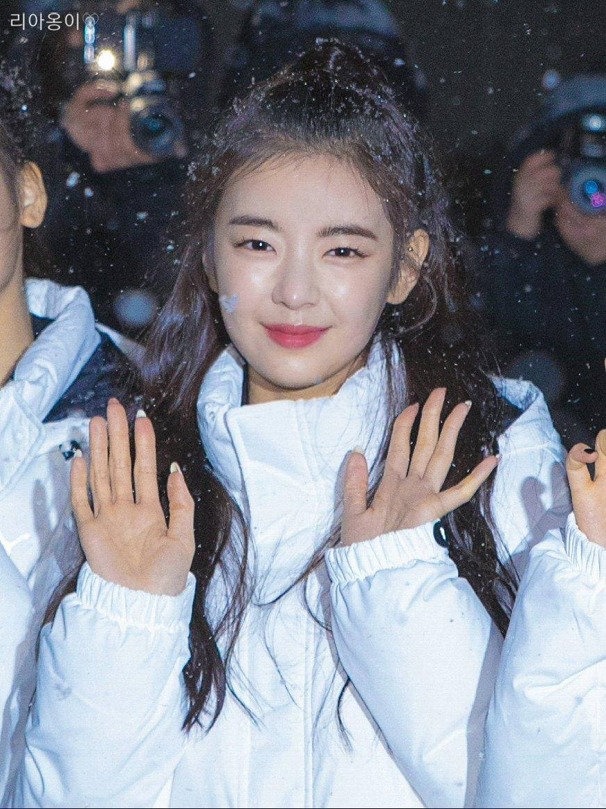 Lia 桌布 壁紙 — 一位年輕女子身穿白色冬季外套，在熙熙攘攘的人群中，雪花飄落，她愉快地揮手。