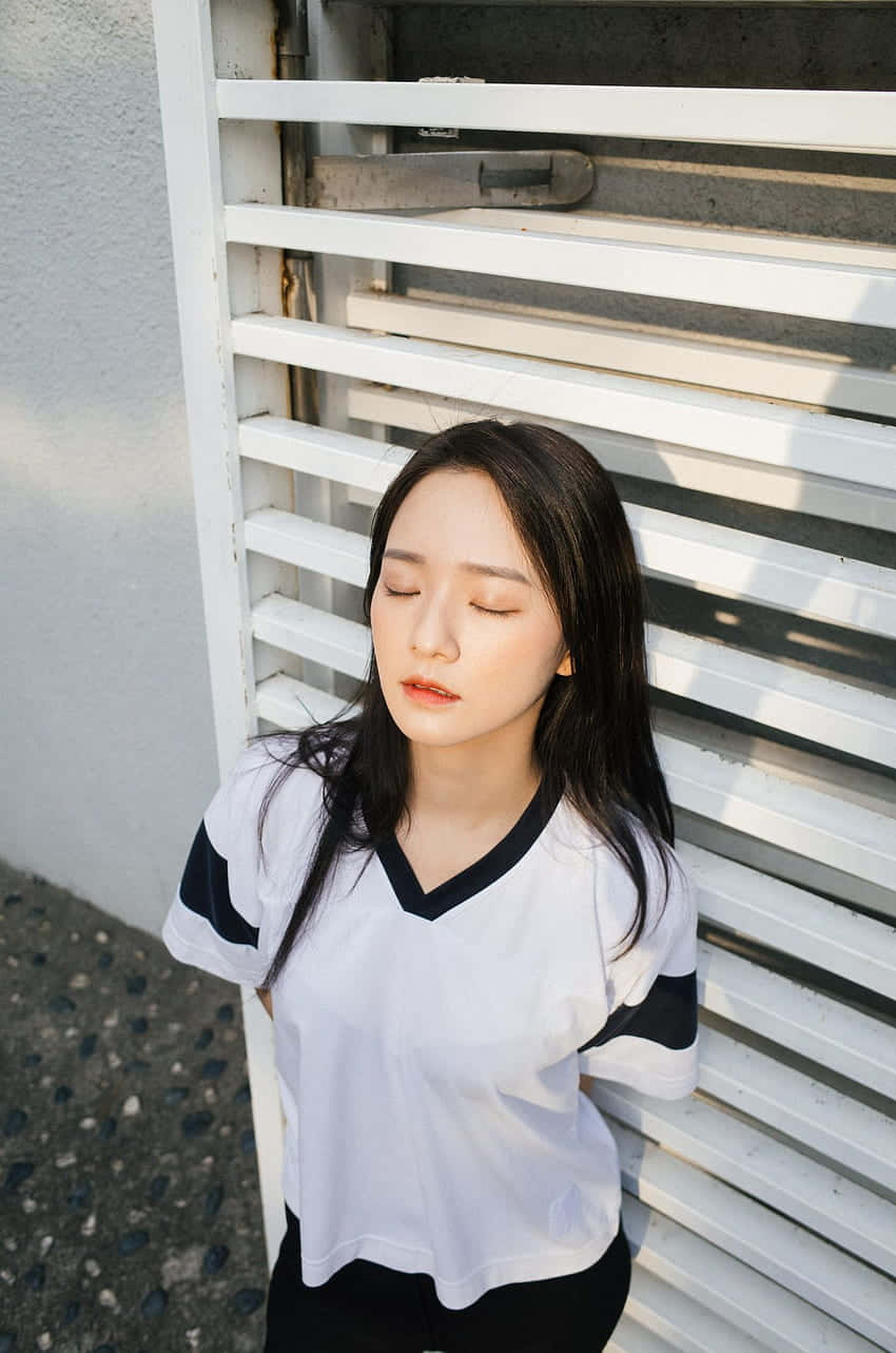 Park Gyu Young 桌布 壁紙 — 一位年輕女子閉著眼睛，靠在沐浴在溫暖金色陽光下的白色百葉窗上。