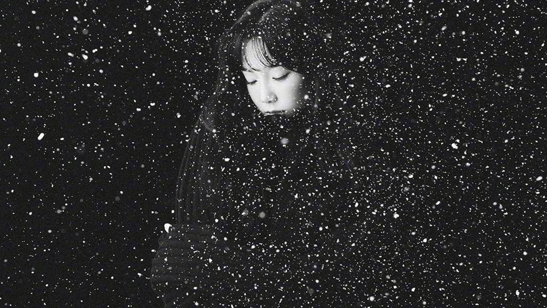 Taeyeon 桌布 壁紙 — 一位年輕女子閉著眼睛站在大雪中，她的臉在黑暗背景下被柔和地照亮。