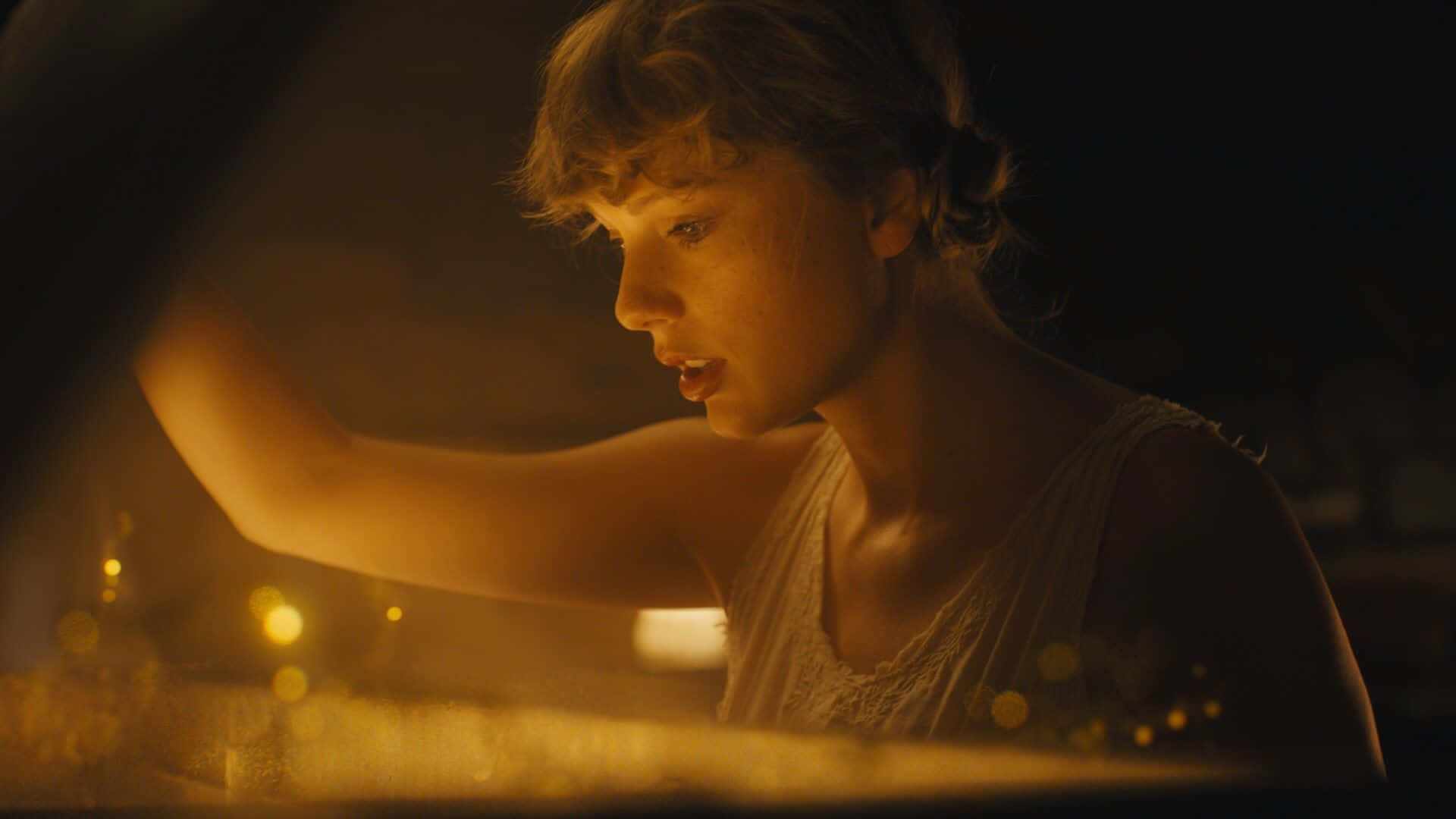 Taylor Swift 桌布 壁紙 — 一位年輕女子頭髮蓬亂，在溫暖的金色光芒中若有所思地凝視著，同時伸手觸摸發光的散景燈光。