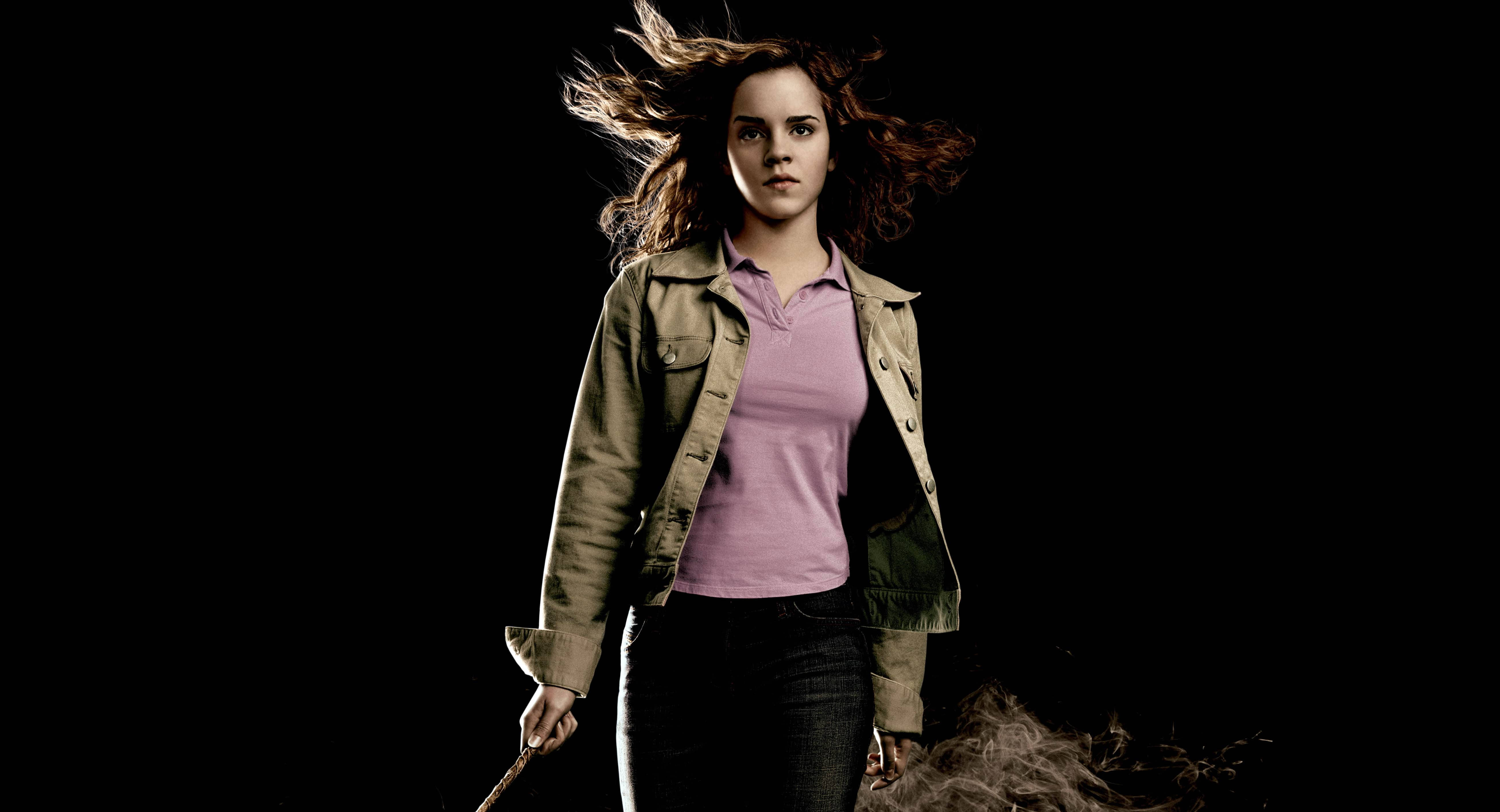 Hermione 桌布 壁紙 — 一位年輕女子頭髮飛揚，手持魔杖，背景是純黑色，腳邊煙霧繚繞。