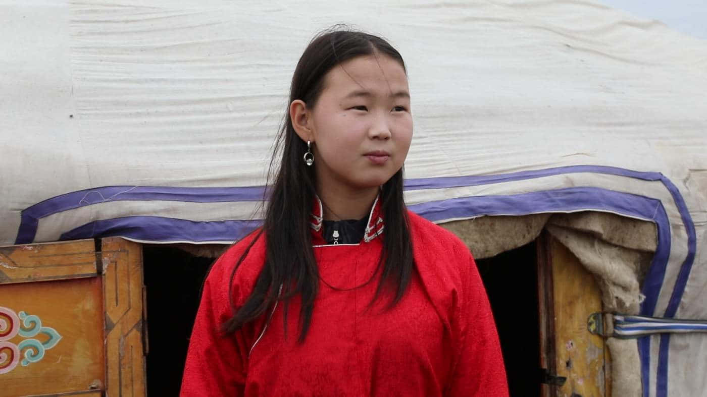 Woman 桌布 壁紙 — 一位年輕女孩穿著鮮豔的紅色傳統服裝，站在一扇有木門和裝飾圖案的風化蒙古包前。