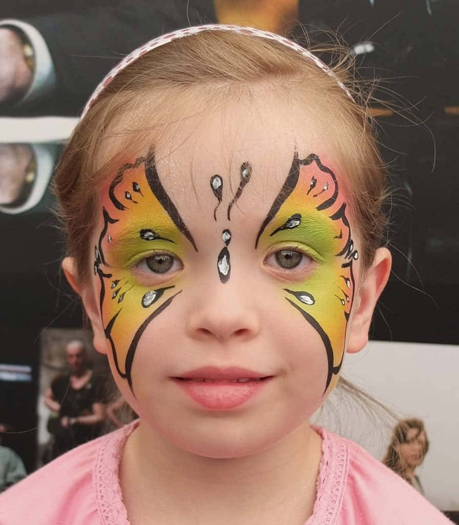 Butterfly Face Painting 桌布 壁紙 — 一位年輕女孩臉上畫著鮮豔的蝴蝶彩繪，在模糊的背景前燦爛微笑。