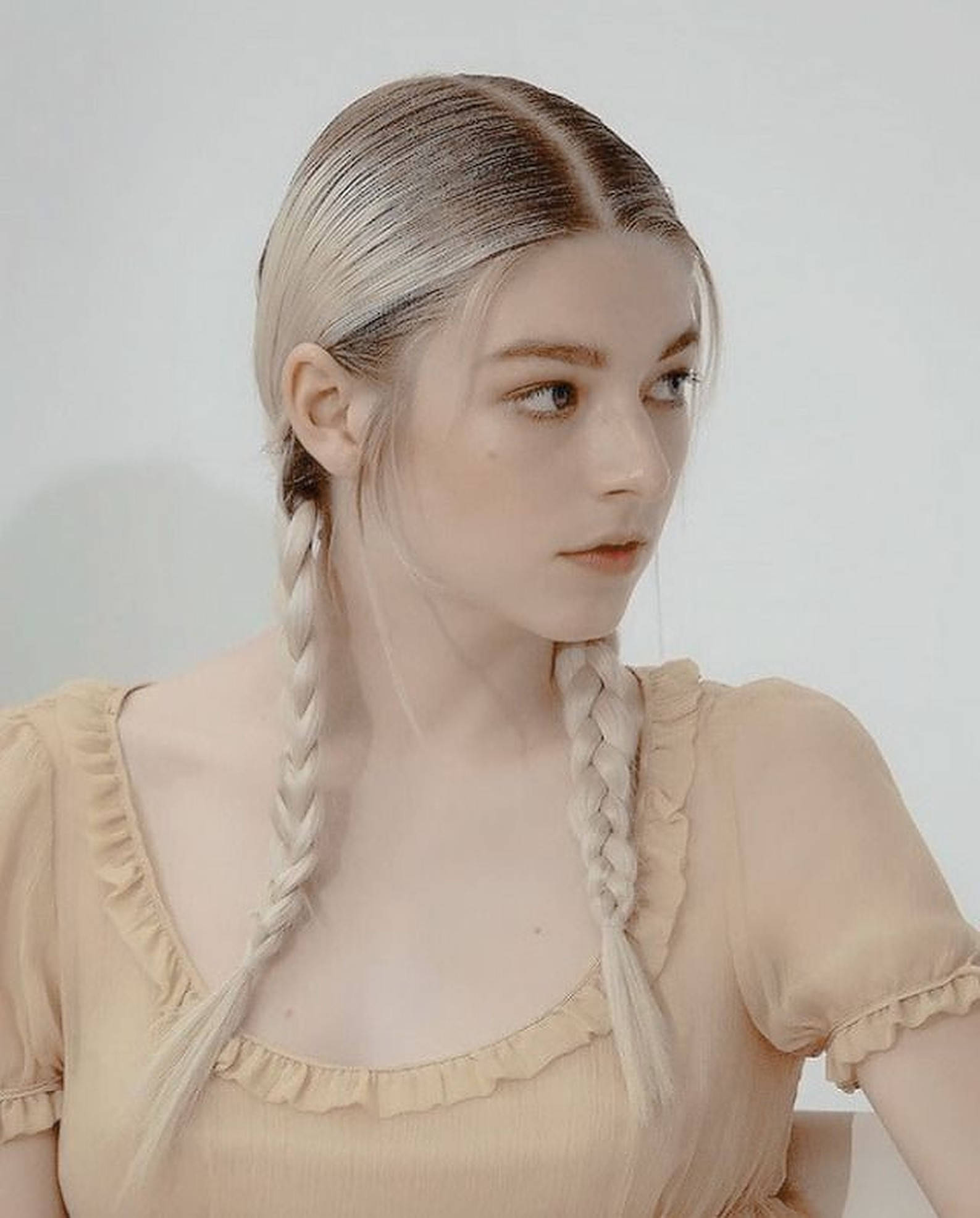 Hunter Schafer 桌布 壁紙 — 一位年輕女性，一頭鉑金色辮子，身穿柔軟米色荷葉邊上衣，背景為純白色。