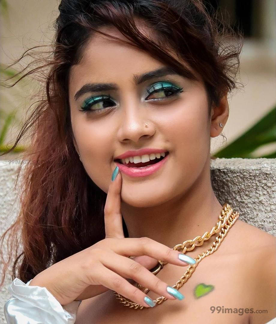 Nisha 桌布 壁紙 — 一位年輕女性，塗著充滿活力的藍綠色眼影和粉紅色嘴唇，微笑著用塗了顏料的手指觸摸臉頰。