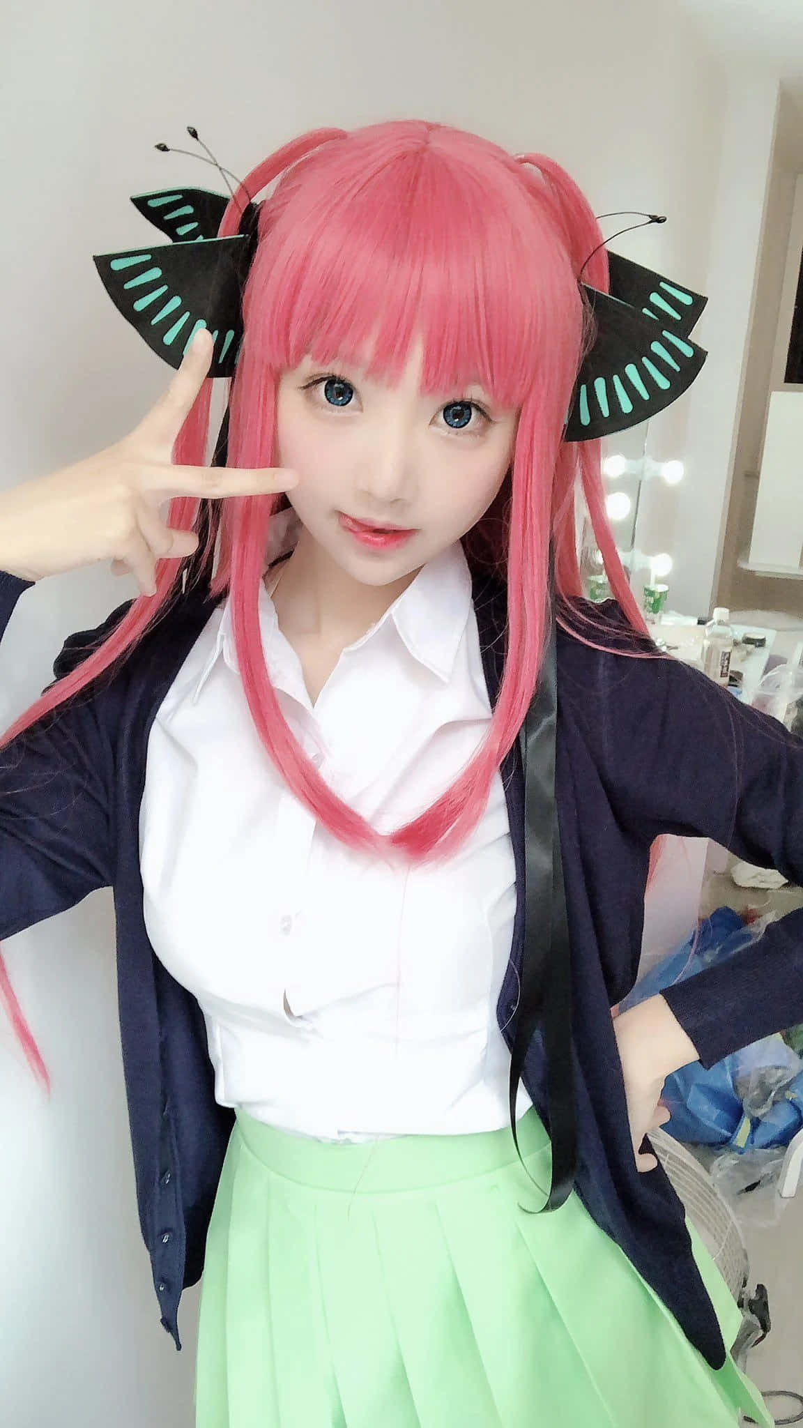 Cosplay Anime Kawaii 桌布 壁紙 — 一位年輕女性，擁有充滿活力的粉紅色頭髮和蝴蝶頭飾，在室內自信地穿著校服擺姿勢。