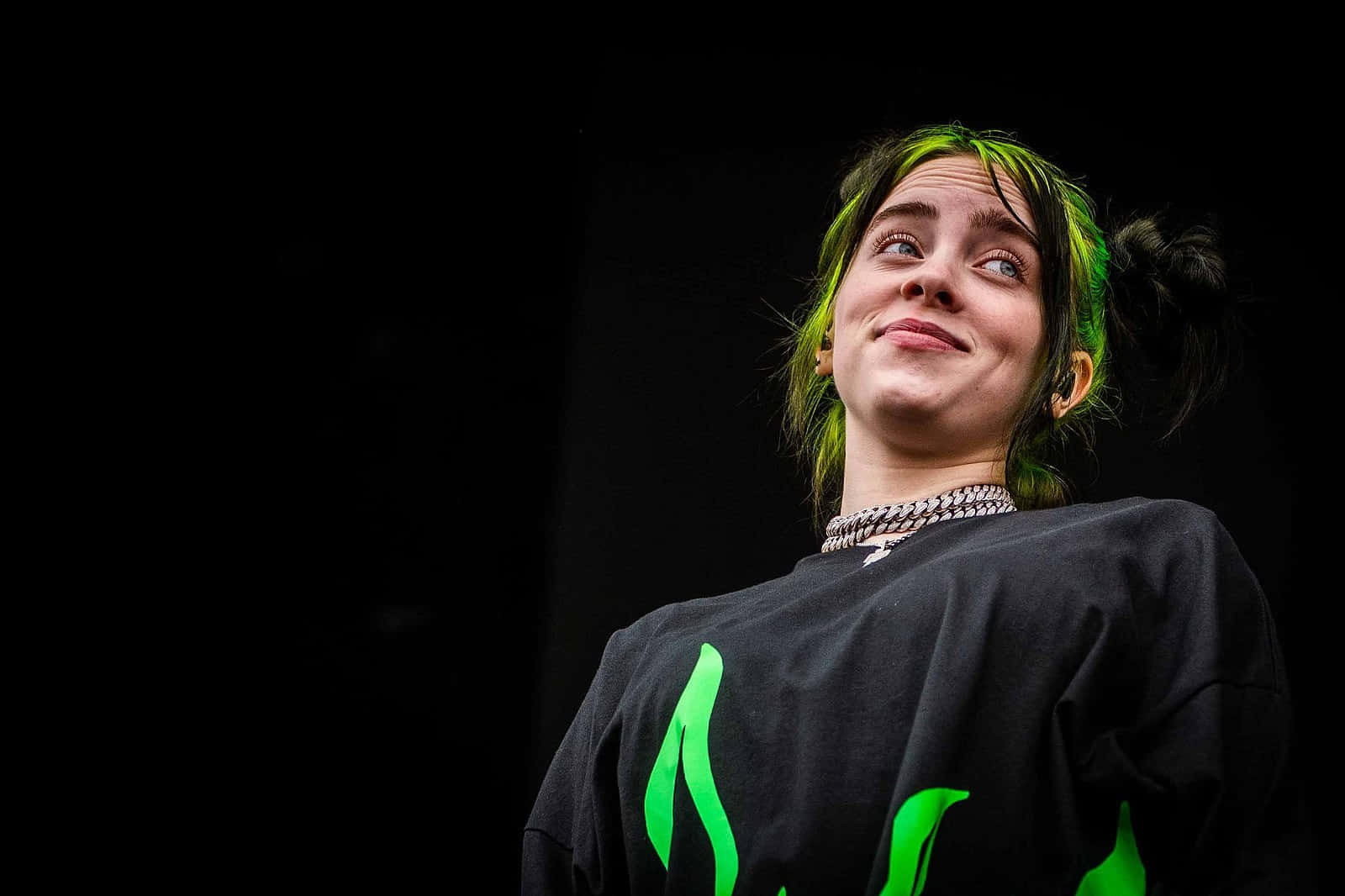 Billie Eilish Laptop 桌布 壁紙 — 一位年輕女性，擁有充滿活力的綠色頭髮，身穿黑色襯衫，在純黑背景上向上微笑。