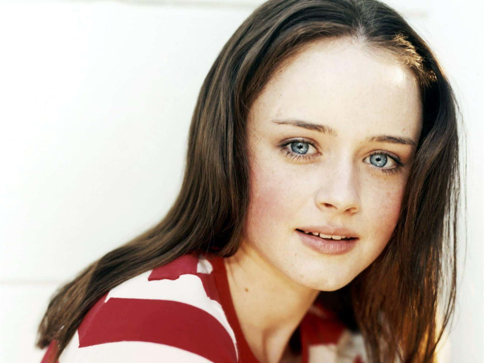 Alexis Bledel 桌布 壁紙 — 一位年輕女性，擁有引人注目的藍色眼睛和雀斑，溫柔地凝視著鏡頭，身穿紅白條紋上衣。