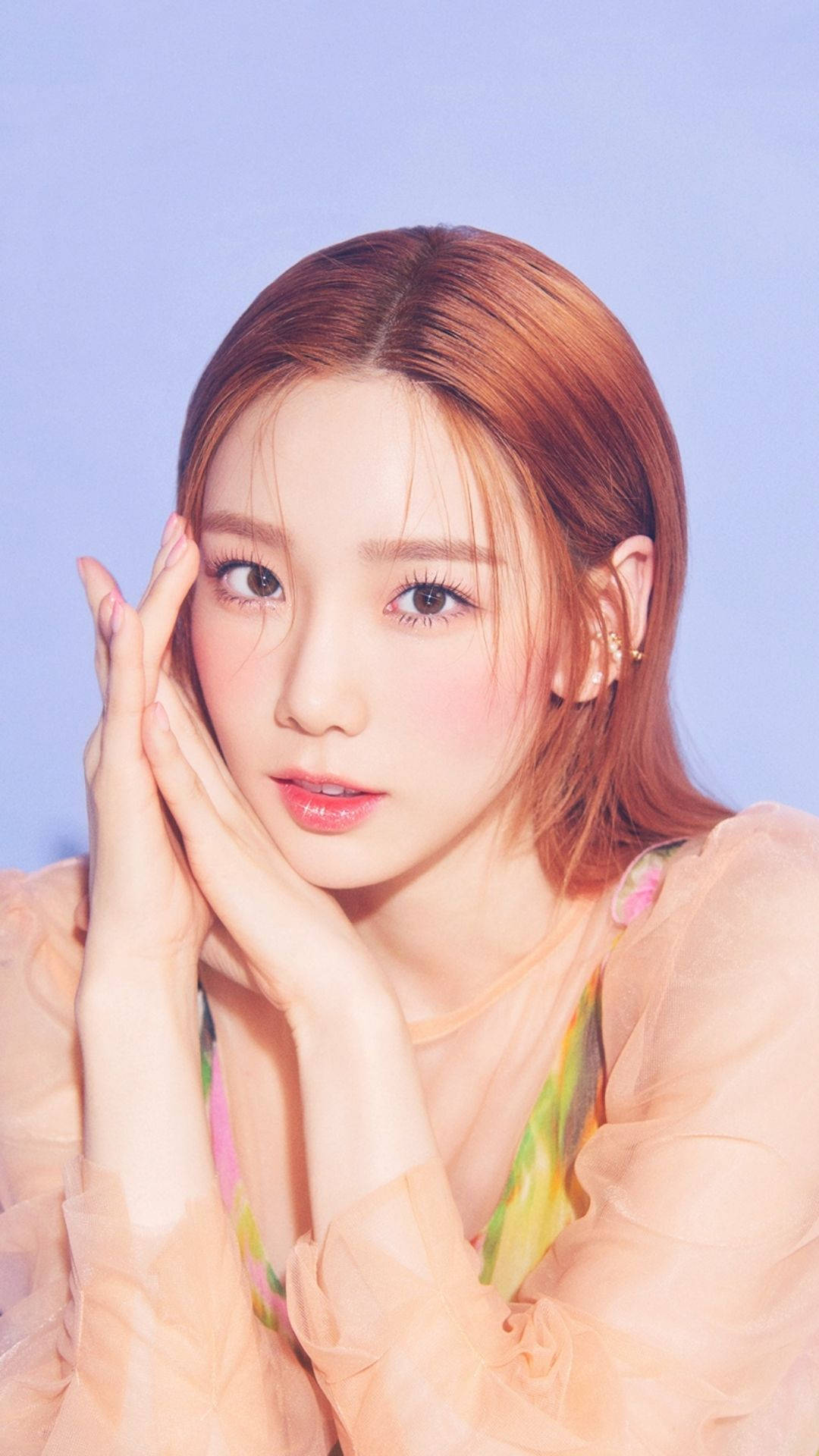 Taeyeon 桌布 壁紙 — 一位年輕女性，擁有暖色調的頭髮，輕輕地將臉頰靠向柔和的薰衣草背景，穿著帶有花卉圖案的透視蜜桃色上衣。