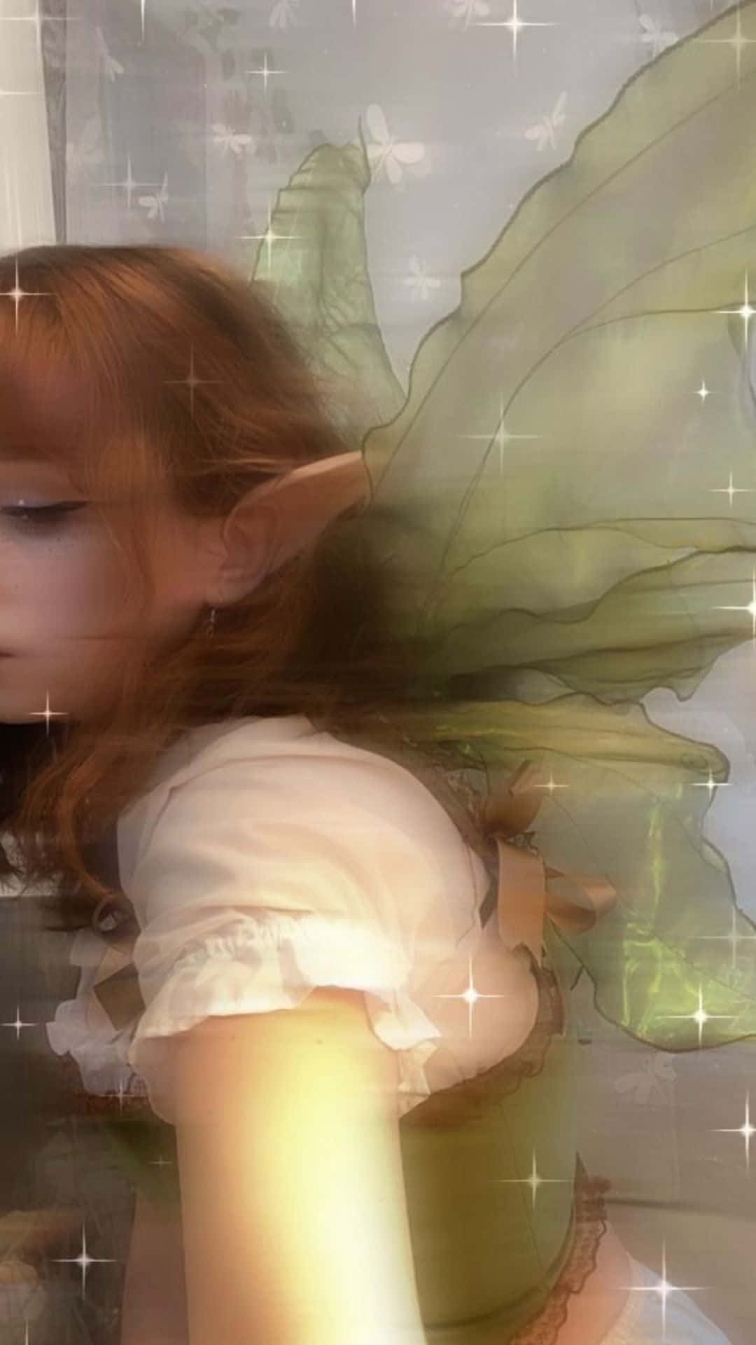 Fairycore 桌布 壁紙 — 一位年輕女性，擁有精靈耳朵和半透明綠色翅膀，在閃爍的發光窗戶前柔和地擺姿勢。