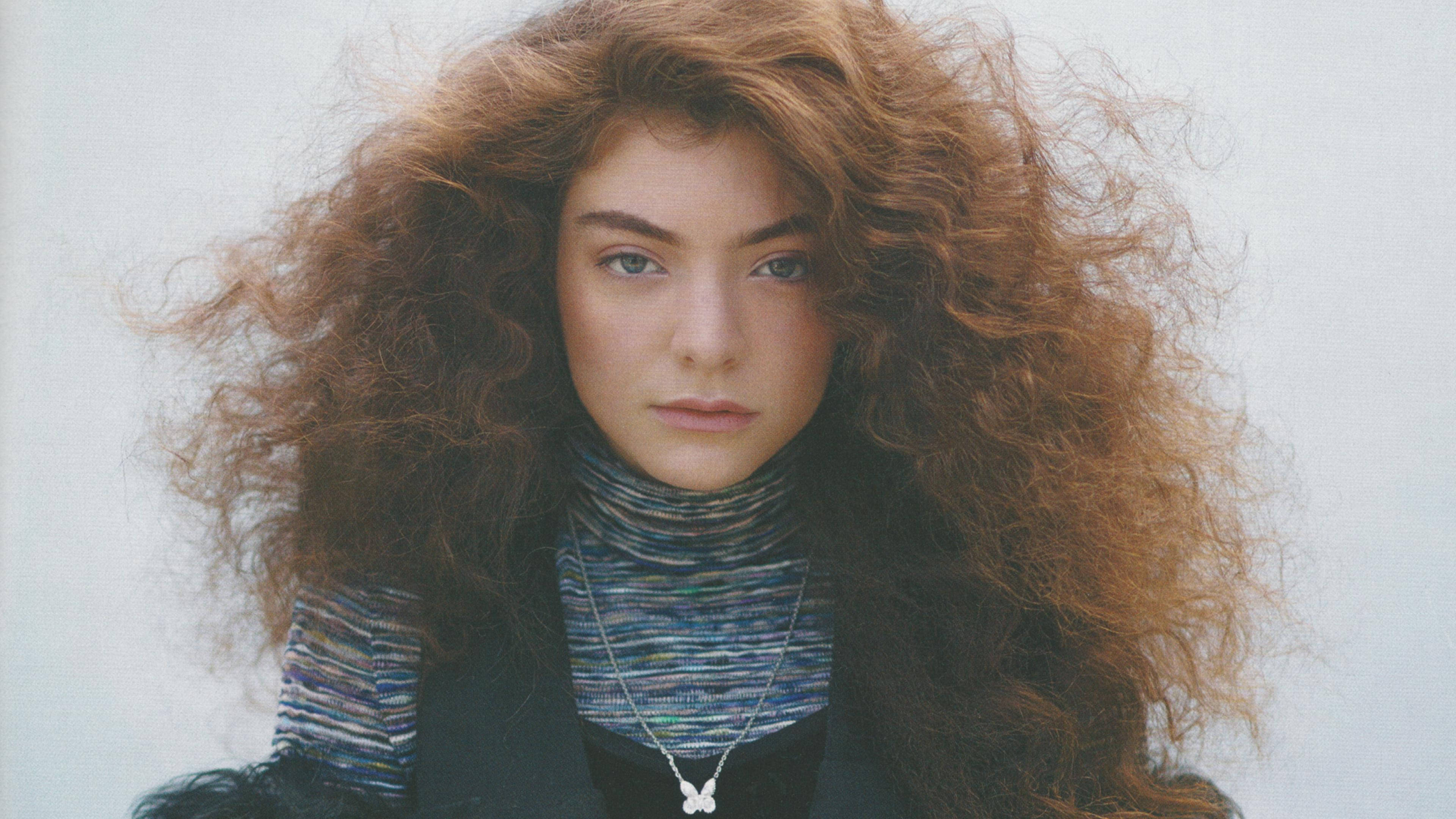 Lorde 桌布 壁紙 — 一位年輕女性，擁有豐盈的捲曲赤褐色頭髮，在純白色背景前直視鏡頭。