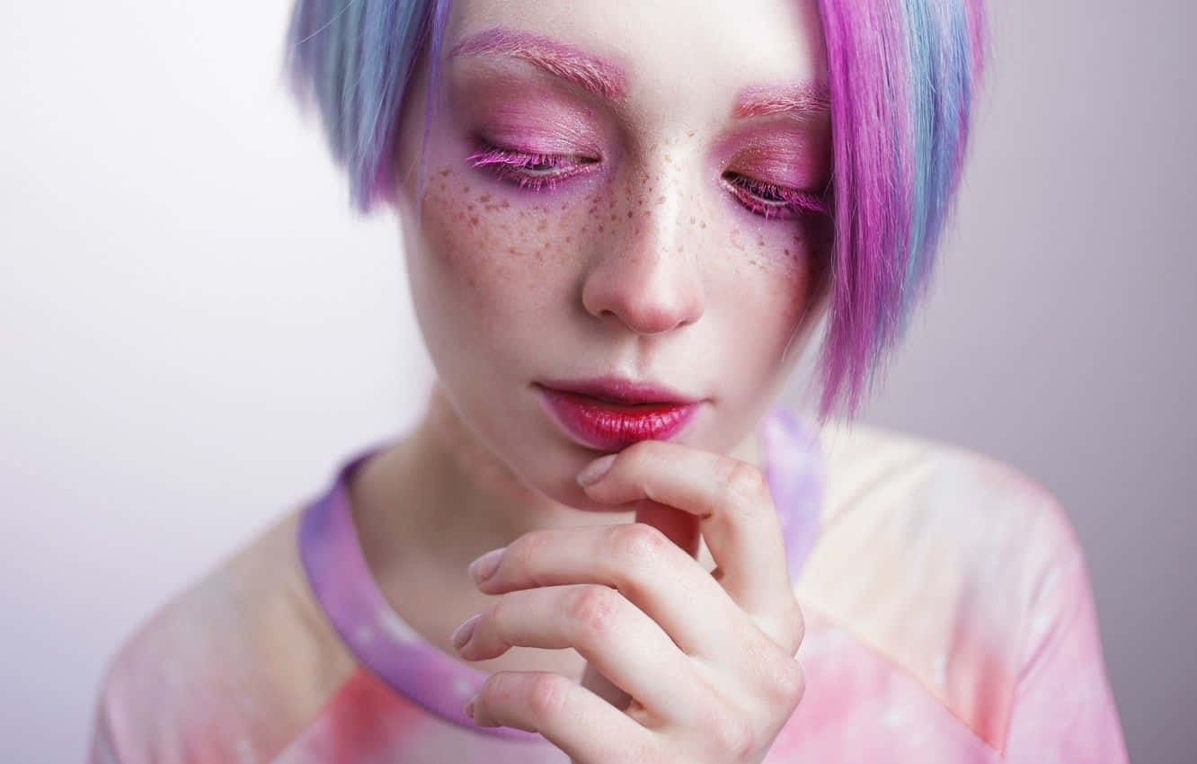 Cute Makeup 桌布 壁紙 — 一位年輕女性，擁有鮮豔的粉紅色和藍色頭髮及雀斑，在柔和的漸變背景上將下巴擱在手上。