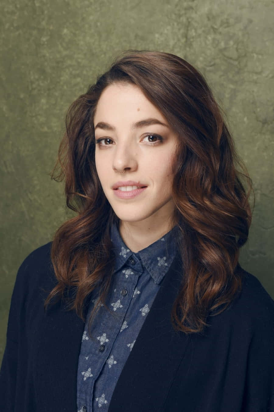 Olivia Thirlby 桌布 壁紙 — 一位年輕女性，波浪棕色頭髮，溫柔微笑，身穿圖案襯衫，外搭深色開襟毛衣，背景為有紋理的橄欖綠色。