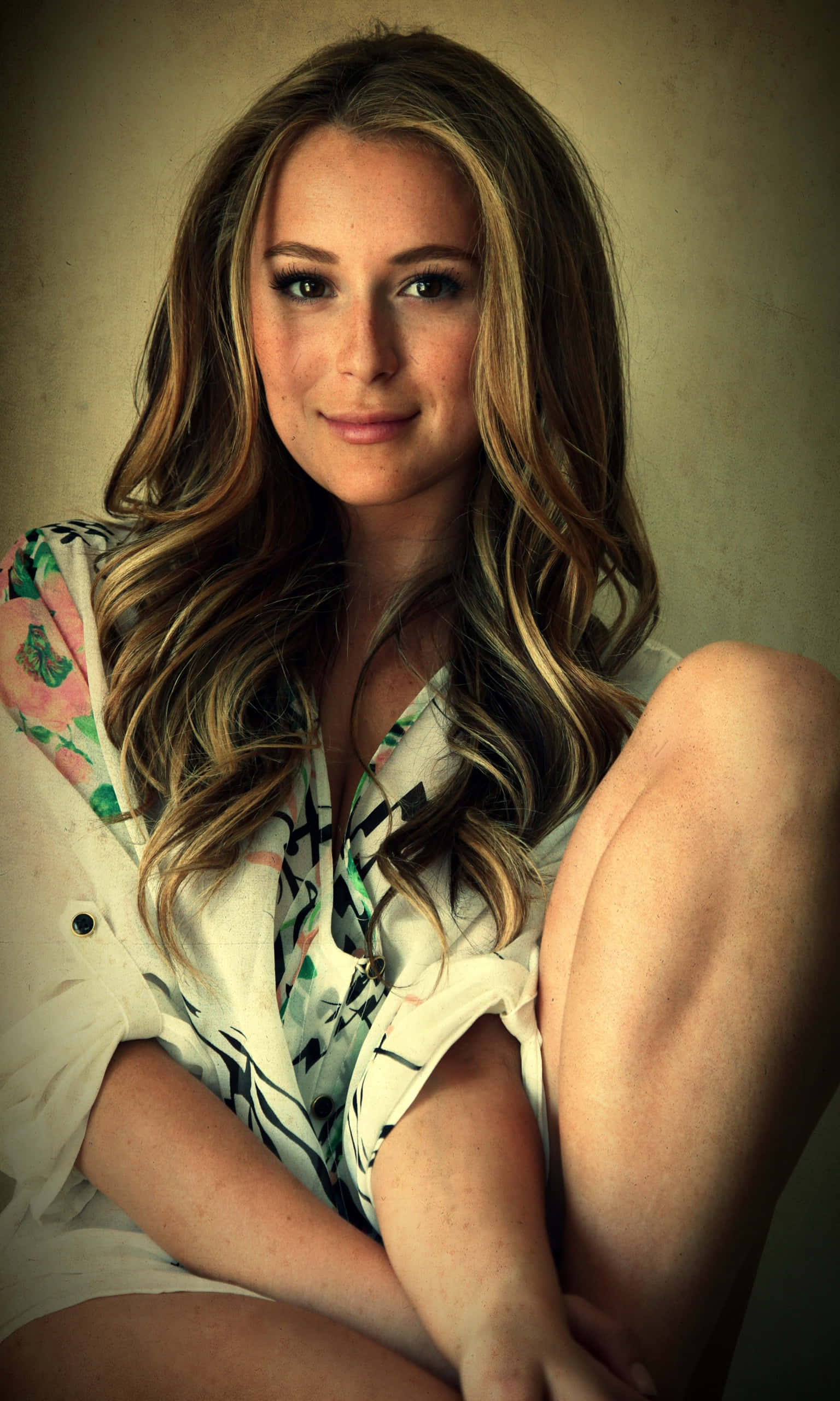 Alexa Penavega 桌布 壁紙 — 一位年輕女性，波浪金髮，靠著質感米色牆壁，穿著圖案襯衫，輕柔微笑。