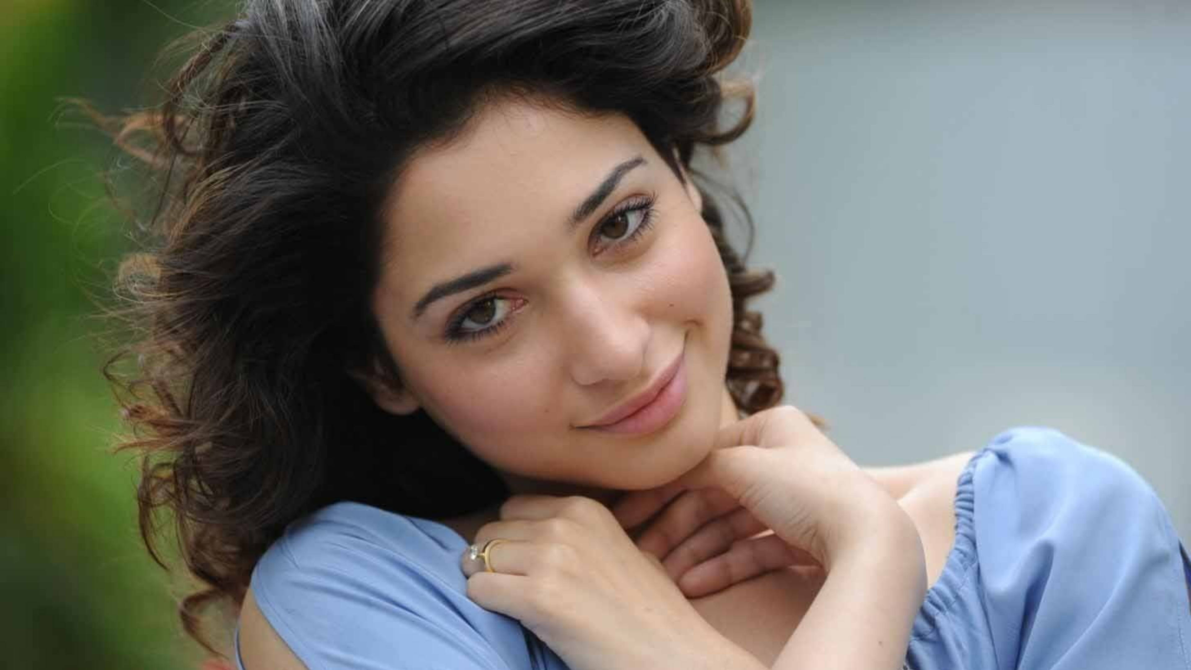tamannaah bhatia 桌布 壁紙 — 一位年輕女性，深色捲髮，穿著淺藍色上衣，雙手托腮，溫柔微笑。