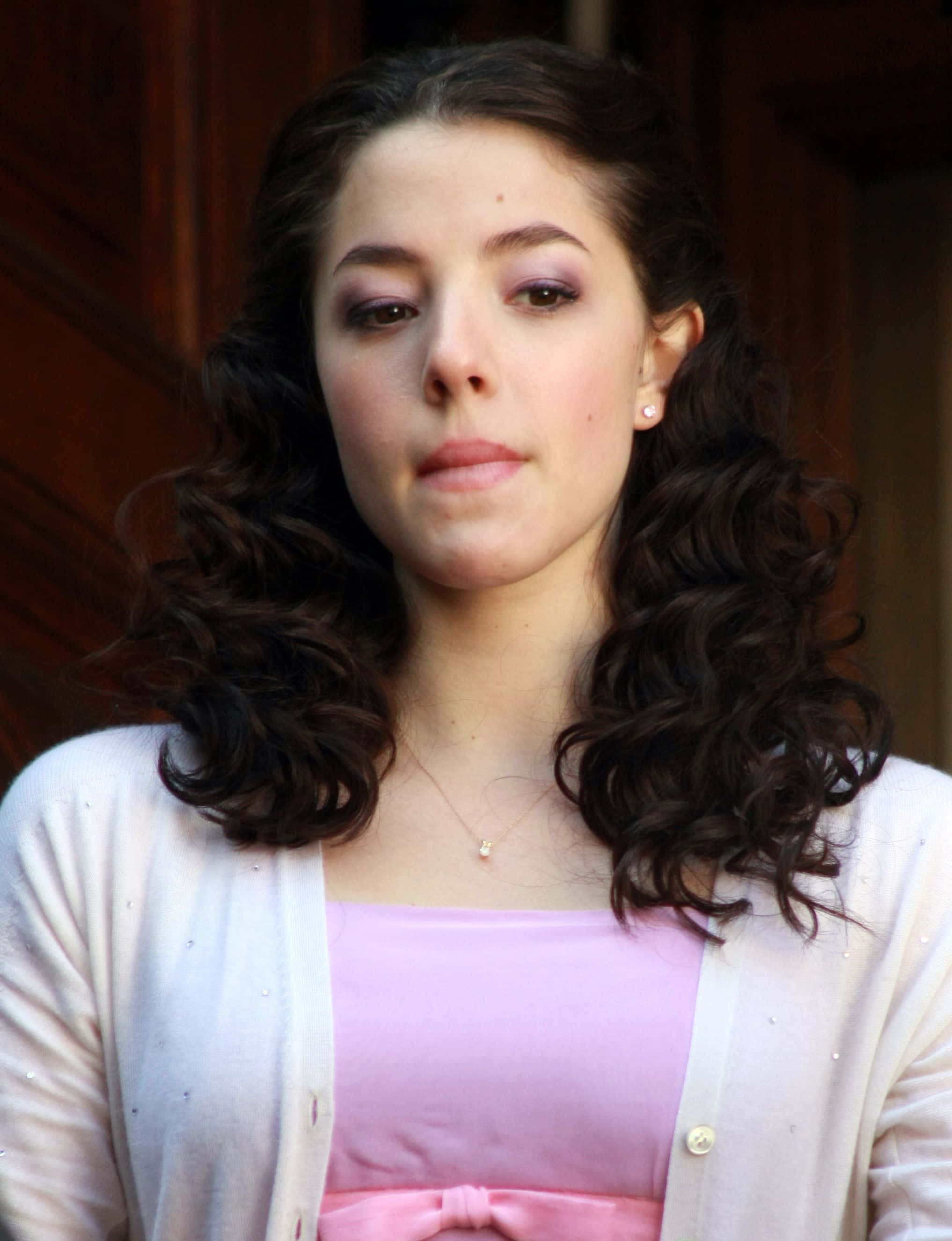 Olivia Thirlby 桌布 壁紙 — 一位年輕女性，深色捲髮，紫色眼影，穿著粉紅色上衣和白色開襟衫，溫柔地凝視著。