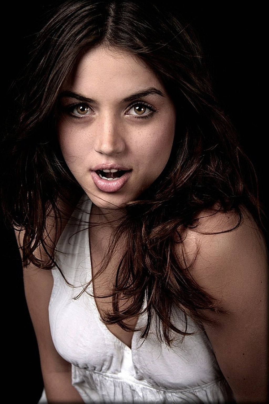 ana de armas 桌布 壁紙 — 一位年輕女性，深色波浪頭髮，眼神富有表現力，在黑色背景前凝視鏡頭。