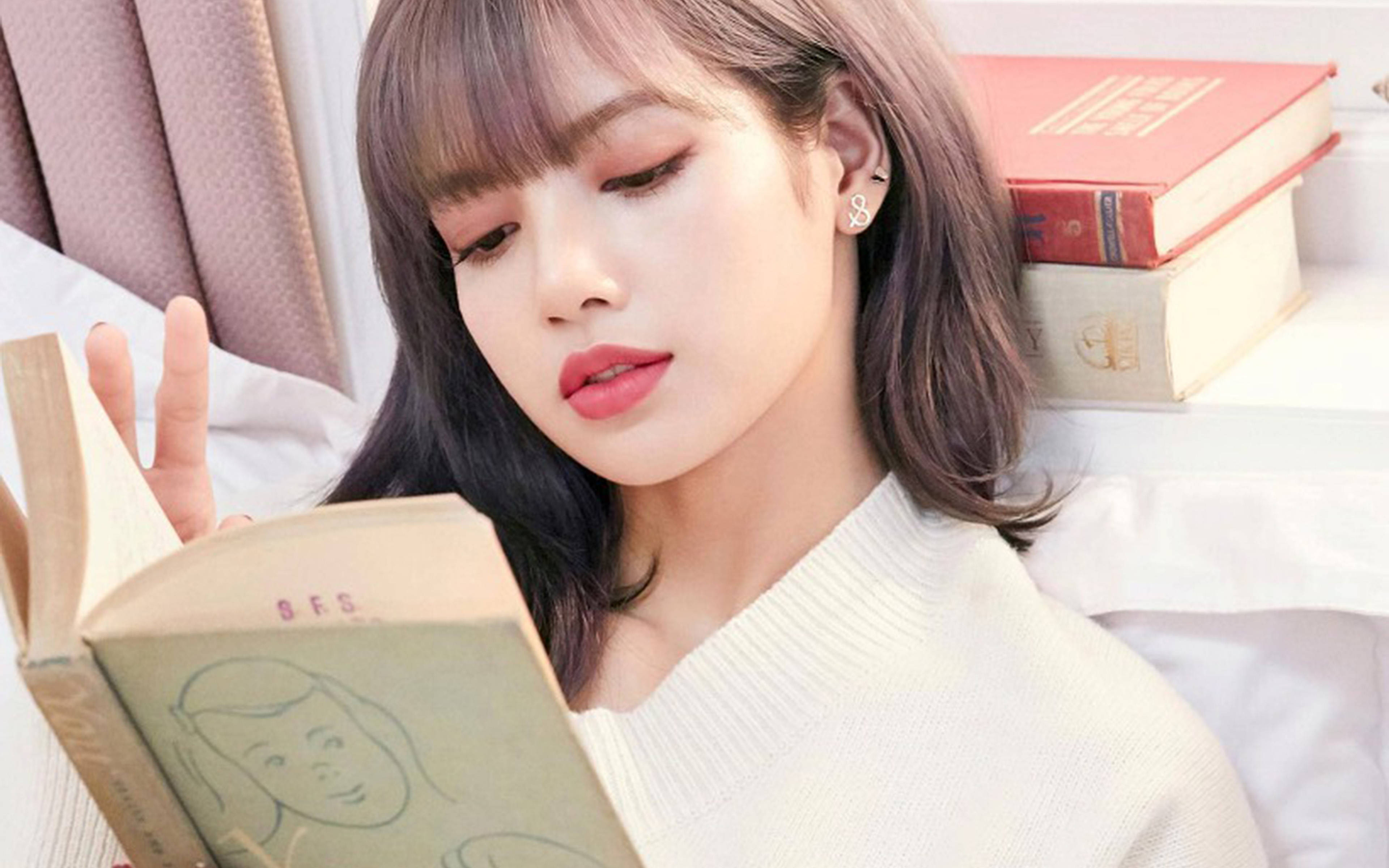 Lalisa 桌布 壁紙 — 一位年輕女性，留著柔軟的劉海和紅唇，躺在一張被堆疊的書籍包圍的床上，閱讀一本復古書籍。