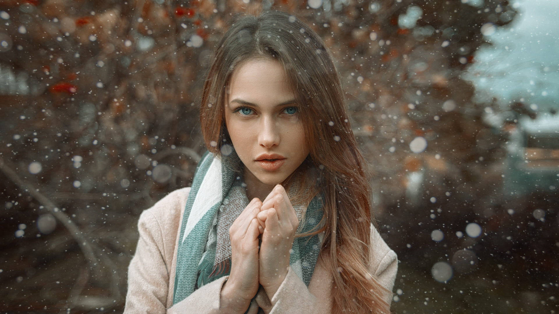 Cute Winter 桌布 壁紙 — 一位年輕女性，藍色眼睛，長長棕色頭髮，站在飄雪中，穿著米色外套和圖案圍巾。