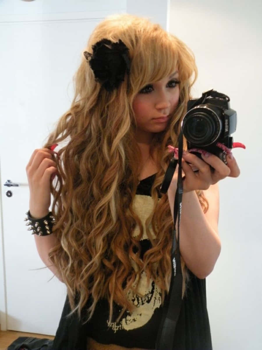Gyaru 桌布 壁紙 — 一位年輕女性，長著波浪形金色長髮，戴著黑色花朵髮夾，在一個樸素的房間裡用單眼相機對著鏡子自拍。