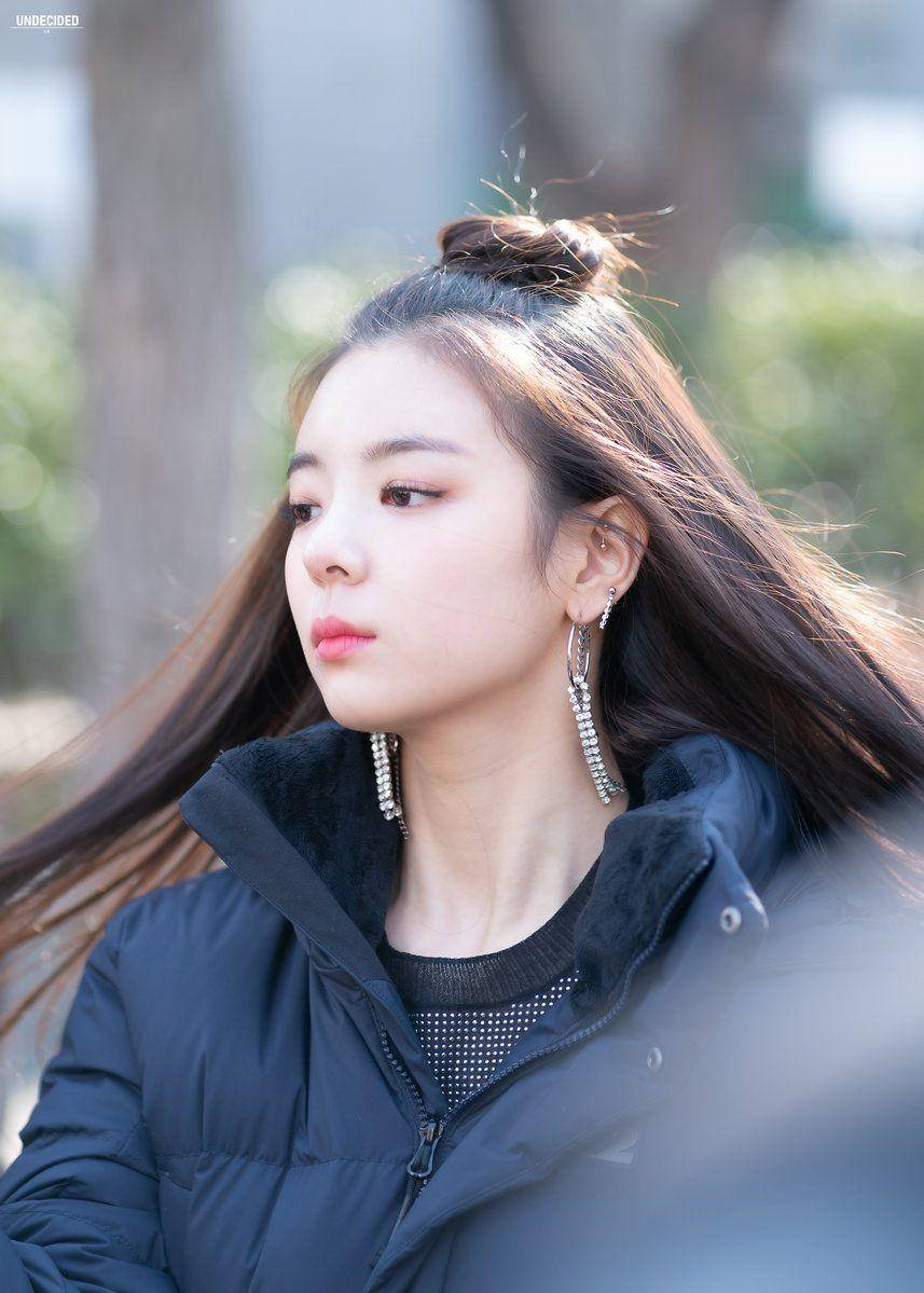 Lia 桌布 壁紙 — 一位年輕女性，長長的棕色頭髮半紮起，在戶外沉思，身穿黑色羽絨外套和垂墜耳環。