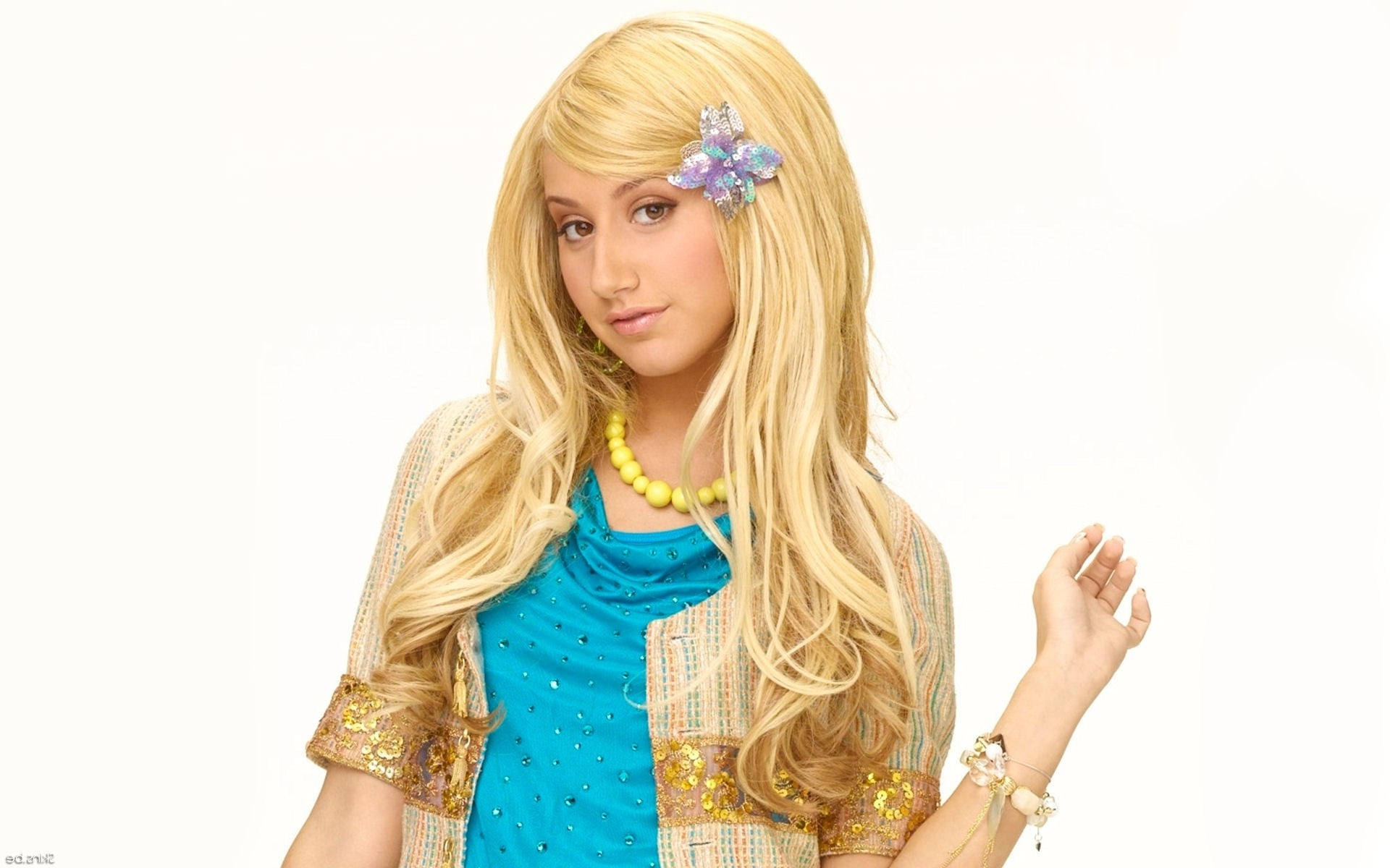 Ashley Tisdale 桌布 壁紙 — 一位年輕女性，長長的金色頭髮上飾有閃亮的花形髮夾，穿著藍色上衣和圖案開襟毛衣，背景為純白色。