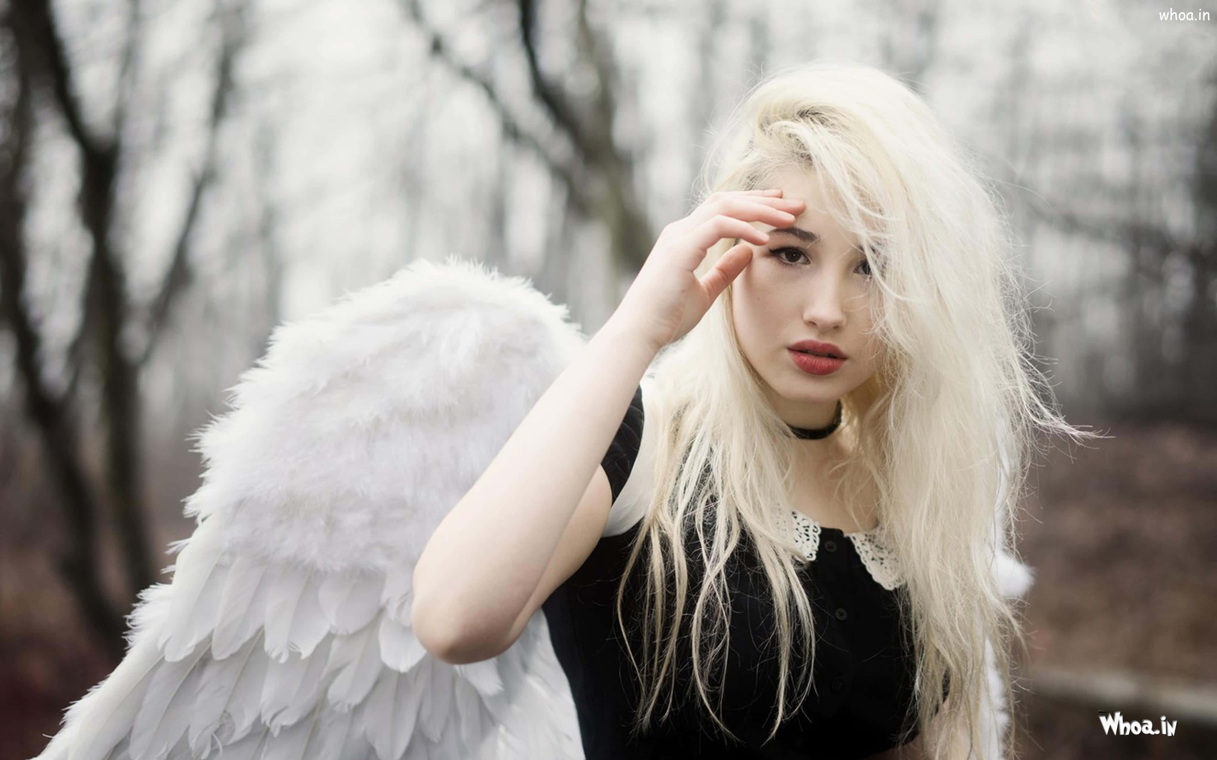 Beautiful Angel 桌布 壁紙 — 一位年輕女性，長長的金色頭髮和巨大的白色天使翅膀，站在光禿禿的冬季森林中，手舉到額頭。