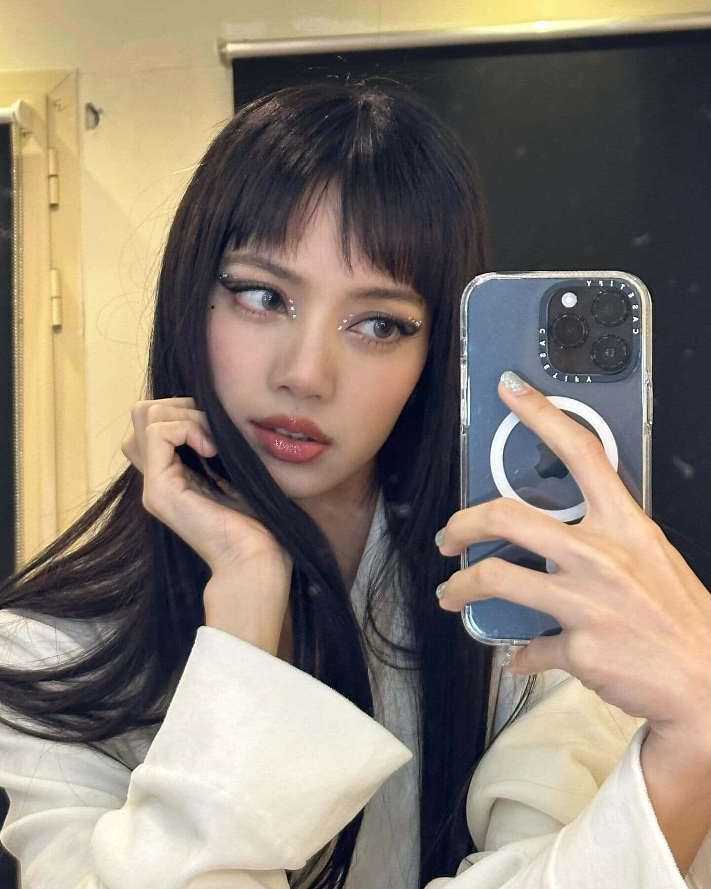 BLACKPINK 桌布 壁紙 — 一位年輕女性，長黑髮，妝容大膽，在柔和光線的室內空間用智慧型手機拍鏡子自拍。