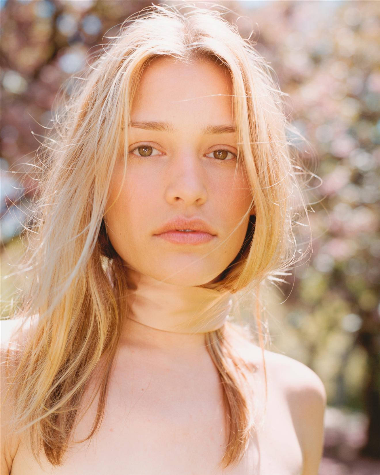 Piper Perabo 桌布 壁紙 — 一位年輕女性，陽光下的金髮，在粉紅花樹的模糊背景下，溫柔地凝視著鏡頭。
