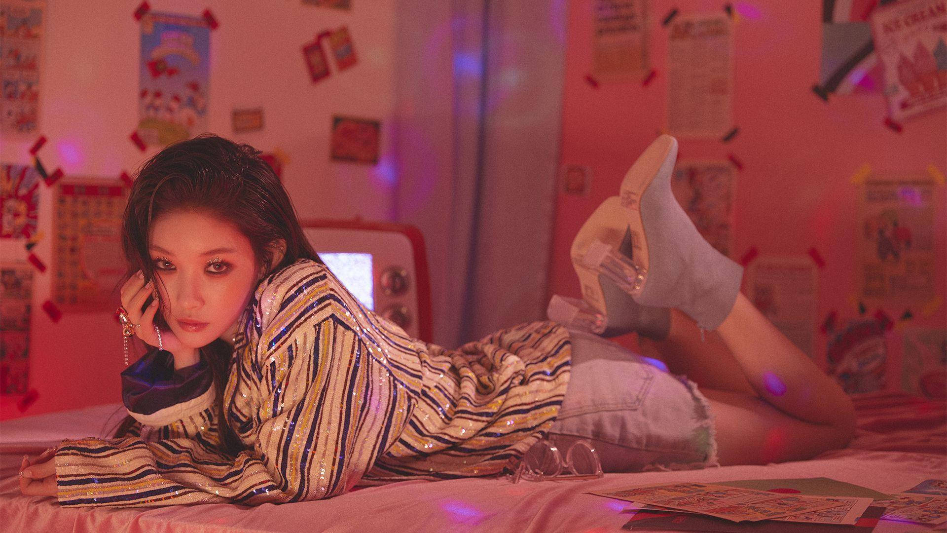 Chungha 桌布 壁紙 — 一位年輕女性在一個充滿海報和紀念品的粉紅色燈光房間裡躺在床上休息。