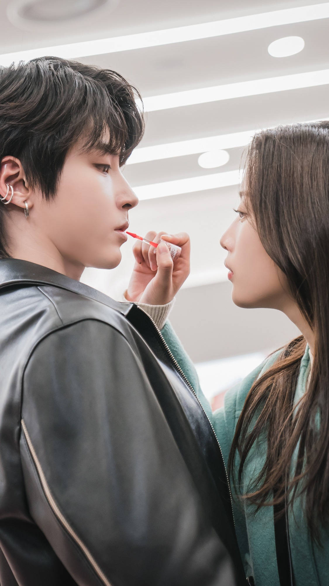 drama 桌布 壁紙 — 一位年輕女性在光線明亮的室內環境中，在現代天花板燈光下，為一名男性塗抹紅色口紅。