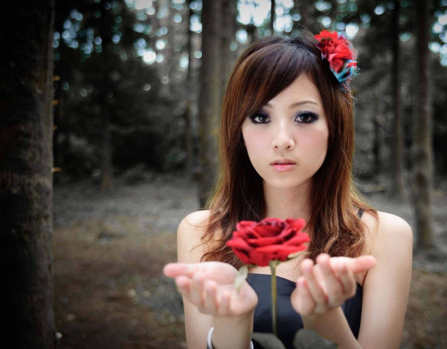 Cute Girl 桌布 壁紙 — 一位年輕女性在森林中，雙手捧著一朵紅玫瑰，表情莊嚴地直視鏡頭。