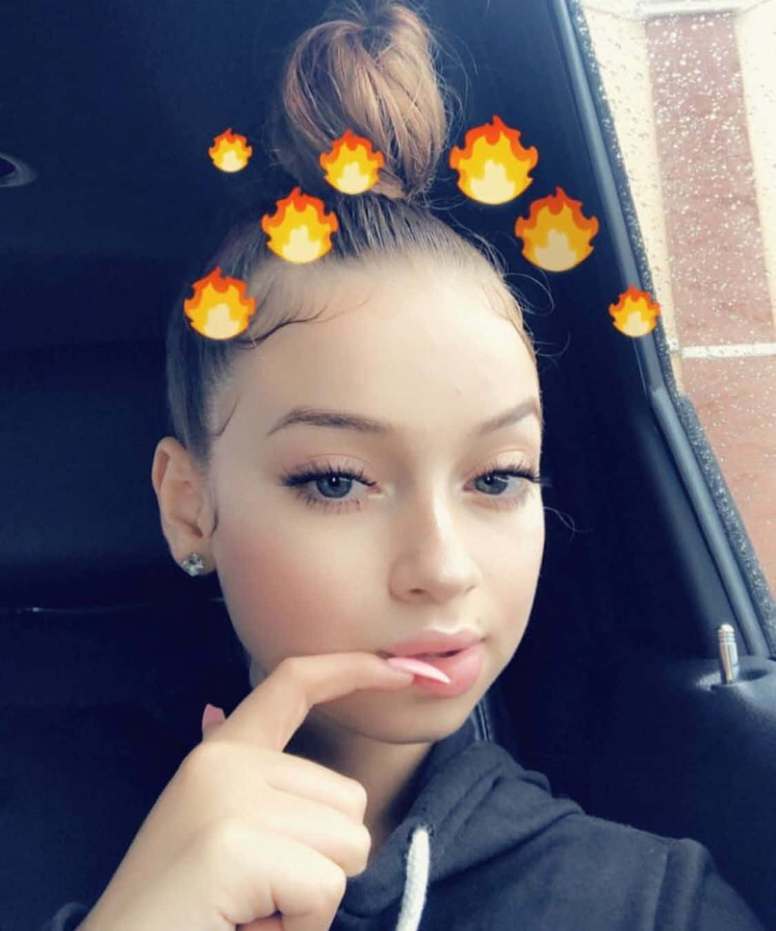 Snapchat 桌布 壁紙 — 一位年輕女性在車內擺姿勢，頭髮紮成火焰表情符號的髮髻，身穿黑色連帽衫。